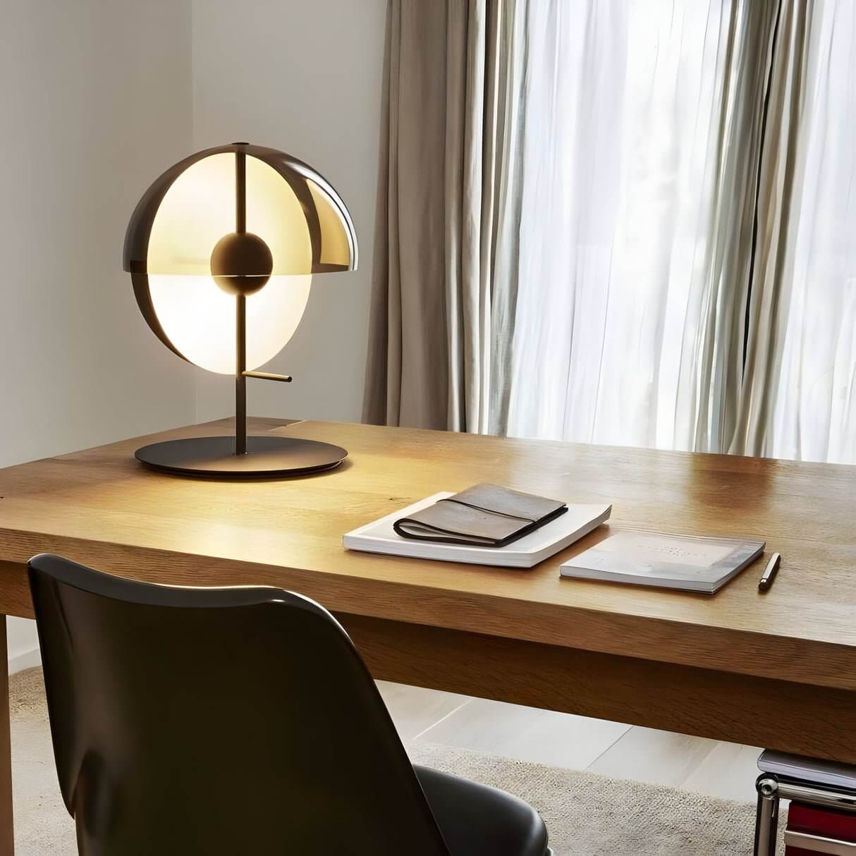 Modern globe-shaped desk lamp glowing on a wooden table in a cozy room with sheer curtains and notebooks.