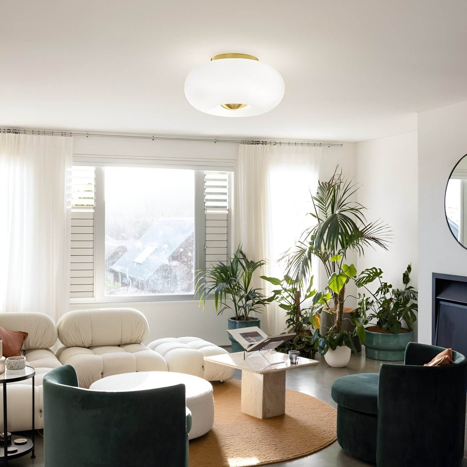Softly lit living room with green velvet chairs, cream sofa, marble table, and brass-accented ceiling light