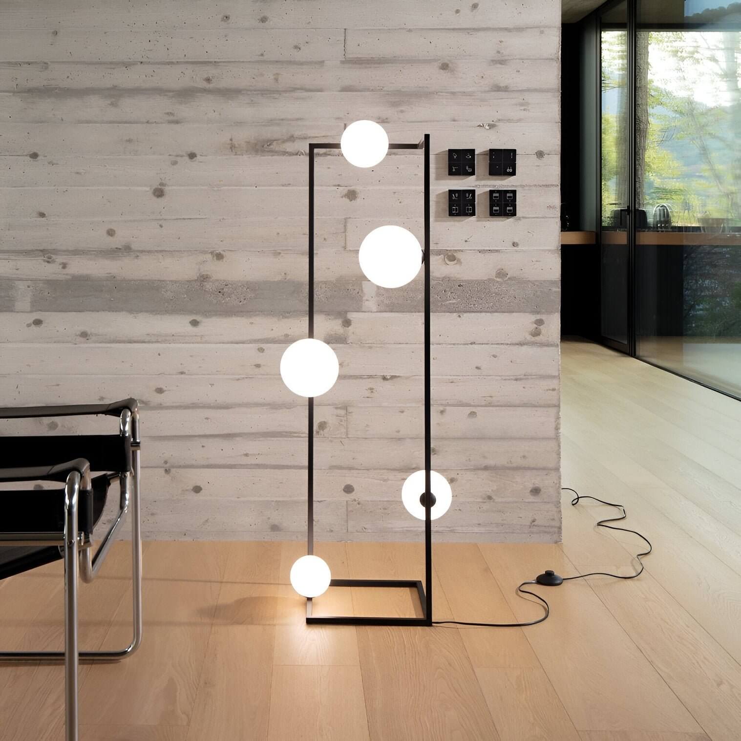Black frame floor lamp with five glowing opal globes arranged vertically in a contemporary interior with concrete walls.