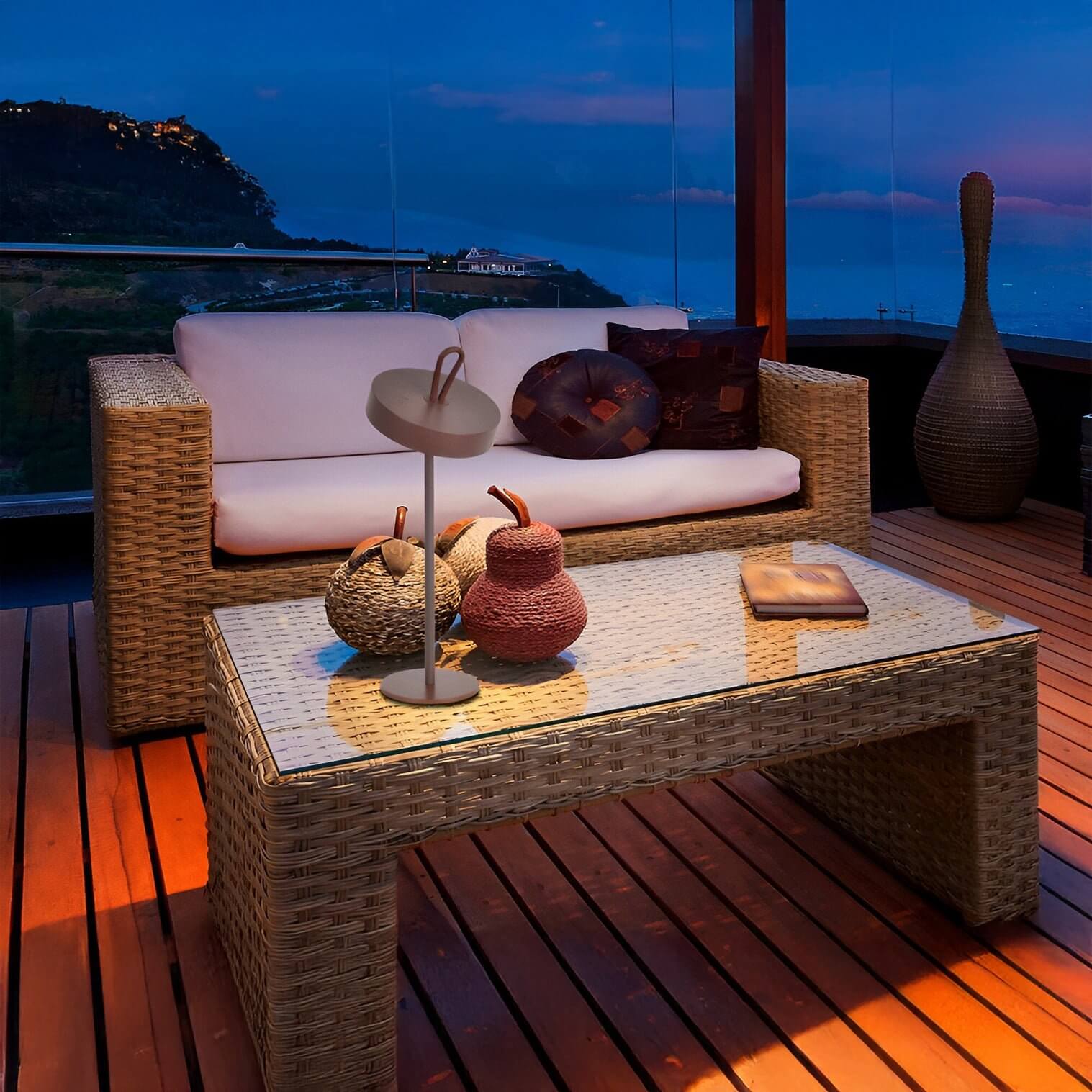 Grey portable LED table lamp with tilted shade on a glass-top wicker table at dusk, styled with natural baskets.