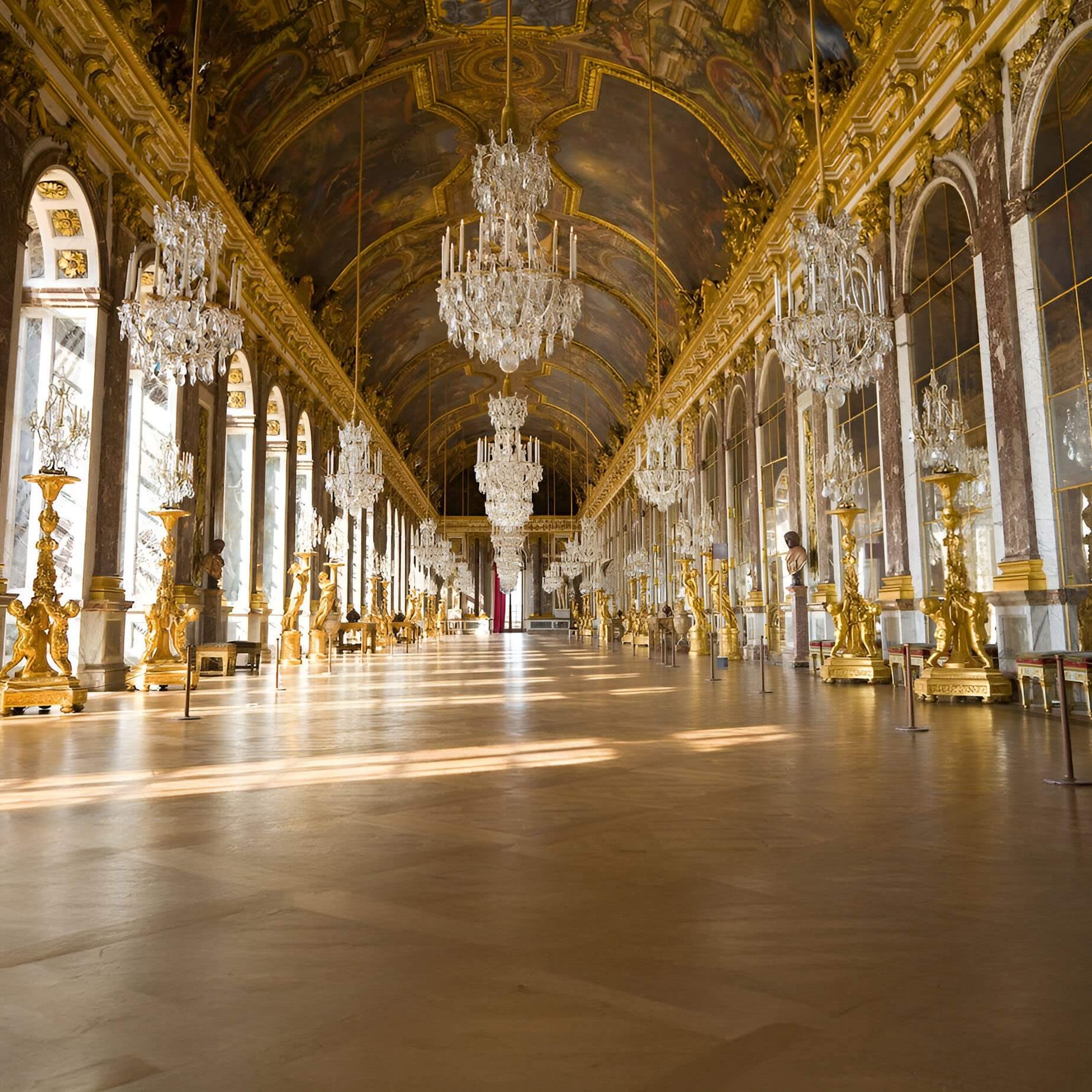 Grand palace hall with gilded décor, mirrored walls, and multiple large crystal chandeliers hanging from a painted ceiling.