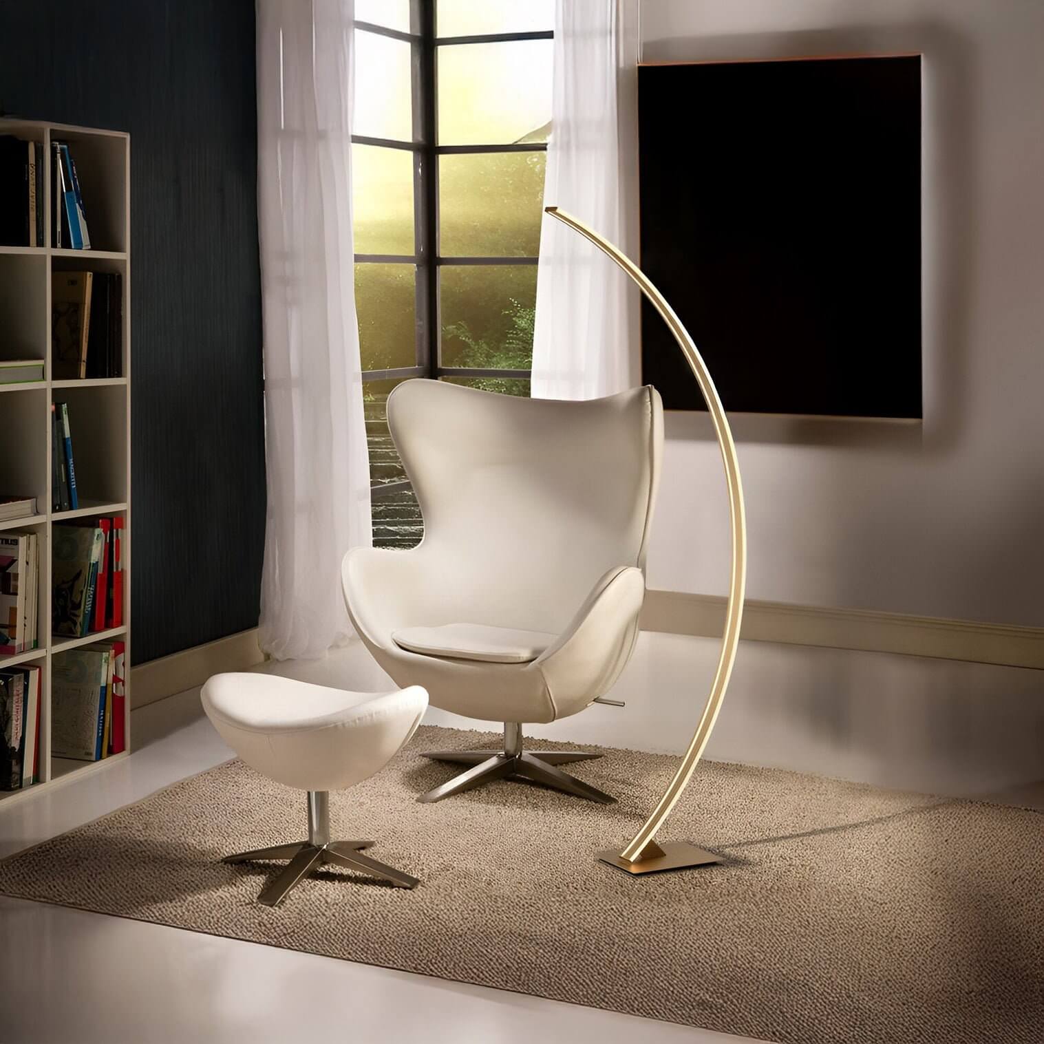 Curved LED floor lamp in brushed gold arches over a white lounge chair in a minimalist, softly lit corner.