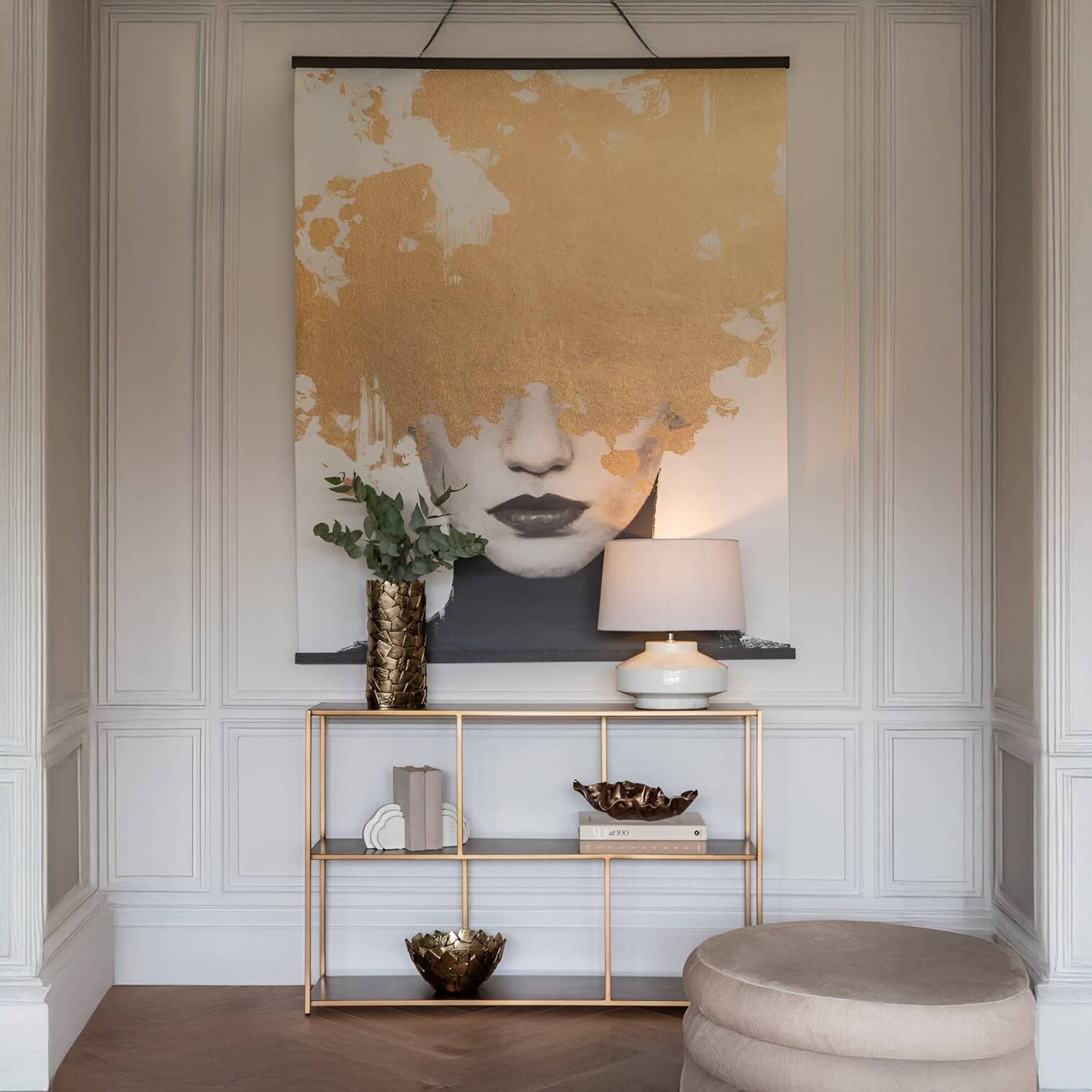 Stylish hallway with a large gold-accent artwork above a slim console table, decorated with a lamp, books, and a textured vase.