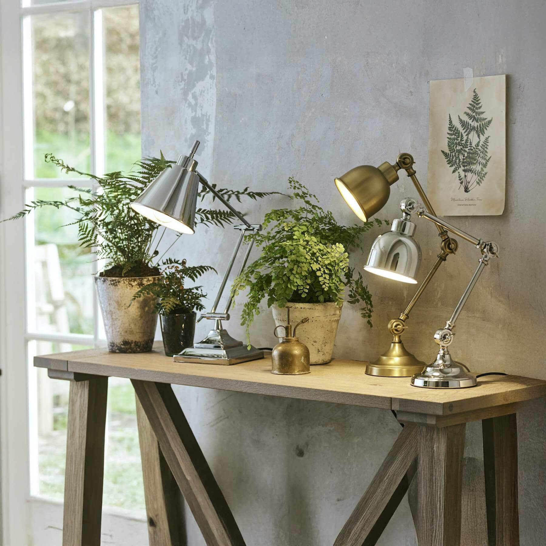 Trio of adjustable industrial desk lamps in silver, brass, and chrome on a rustic wooden console.