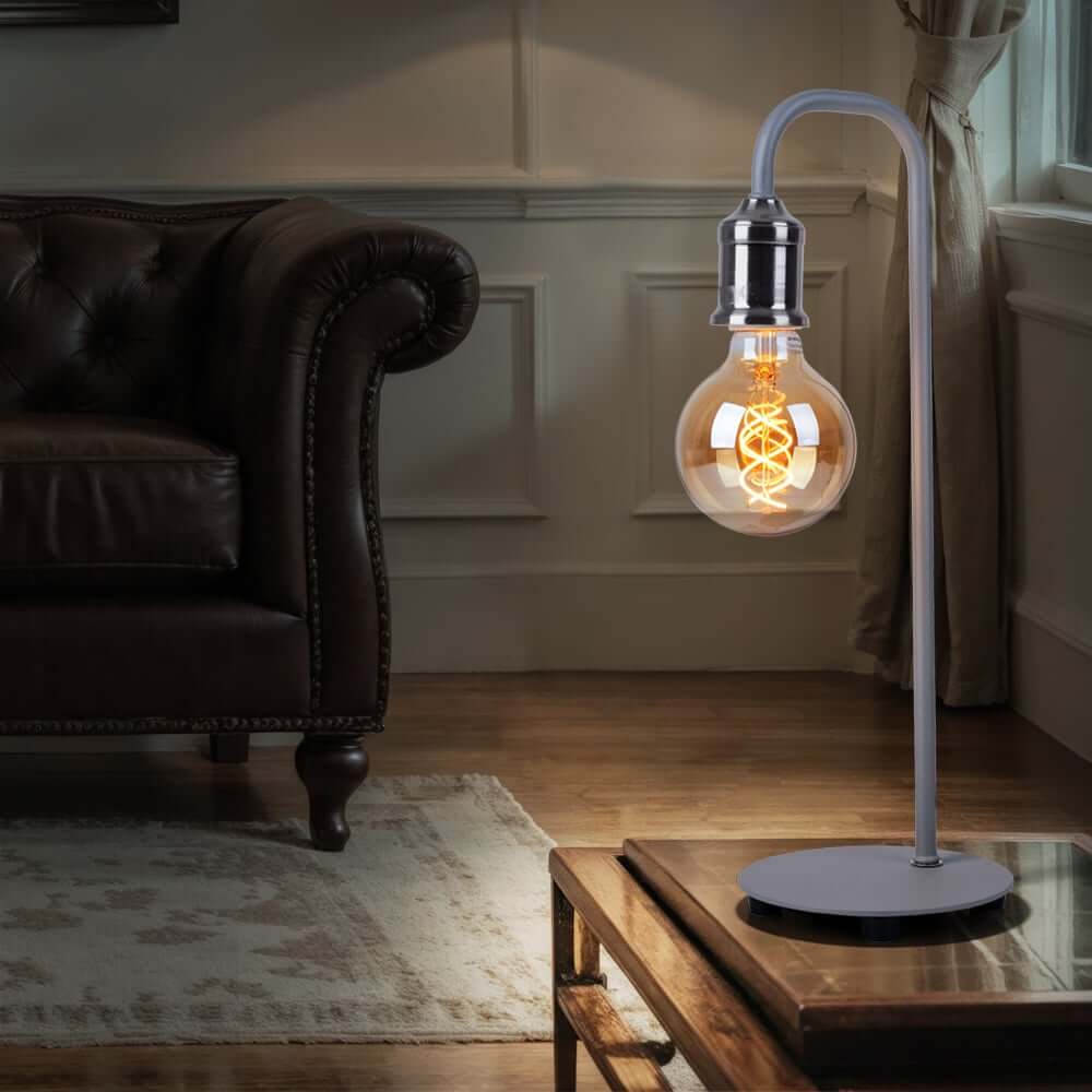 Modern table lamp with exposed Edison bulb and curved metal stand on a glass coffee table.