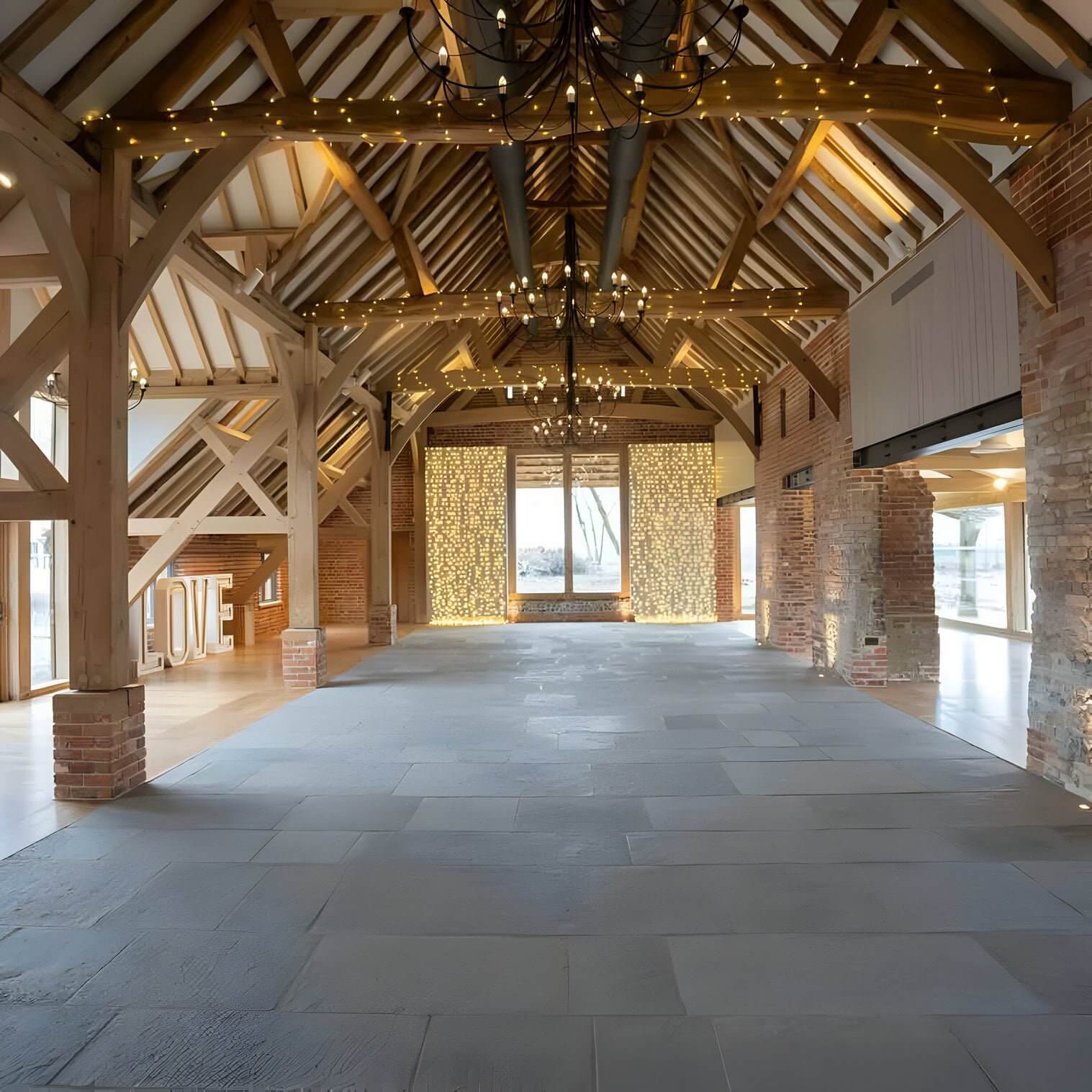 Black wrought iron chandeliers with fairy lights in a vaulted timber-framed barn interior.