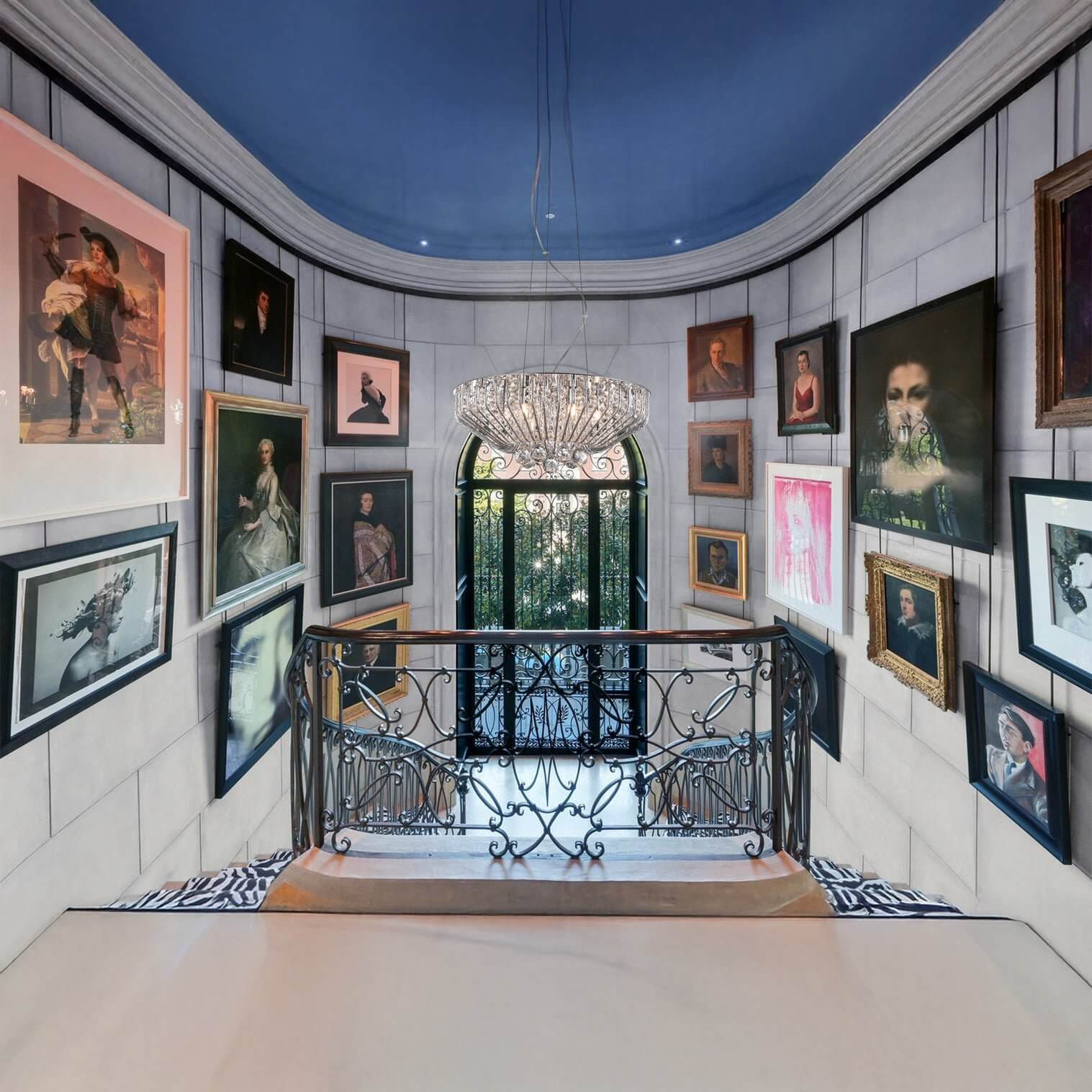 Artistic hallway with framed portraits and a dramatic crystal chandelier above the staircase.