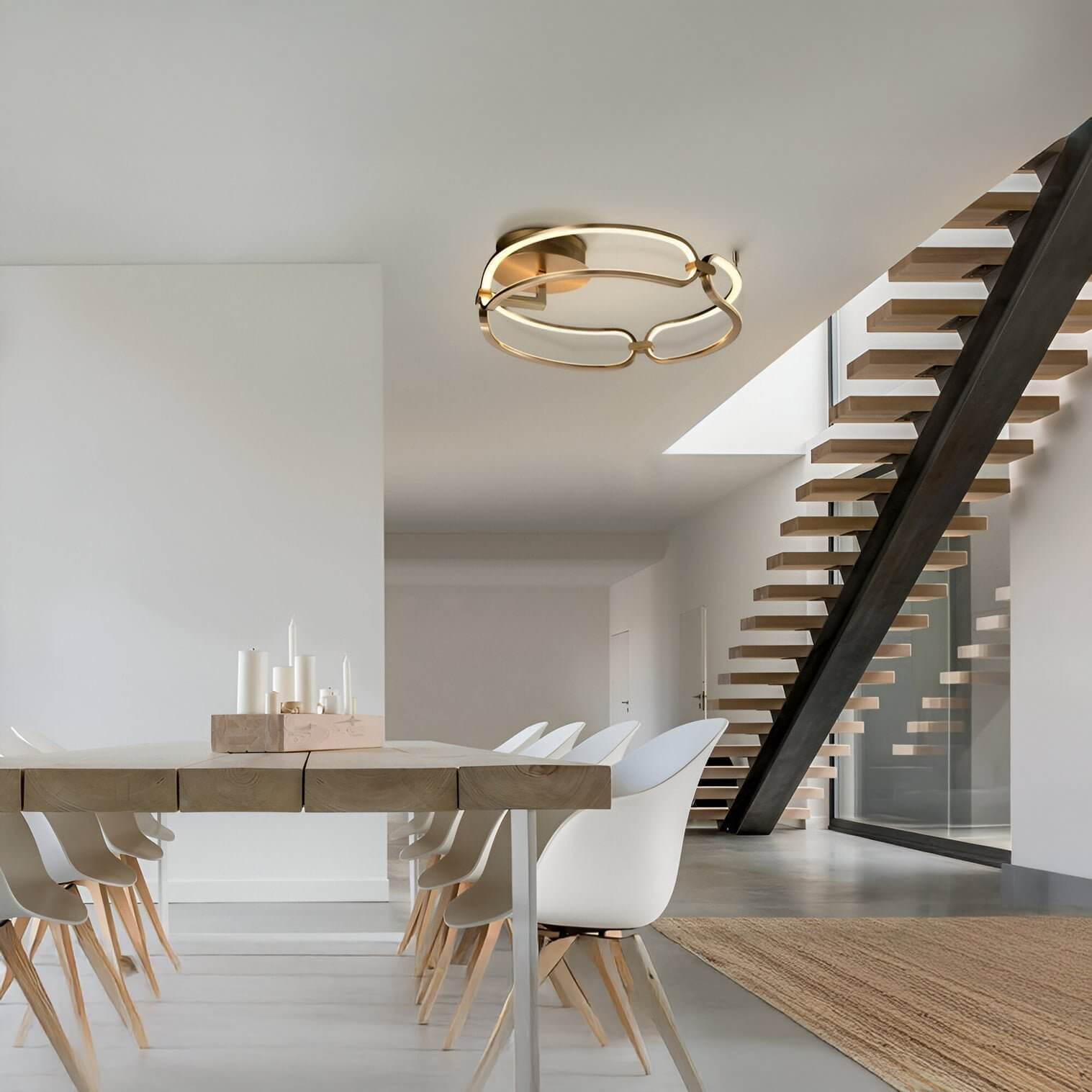 Sculptural gold ceiling light with organic loop design in a minimalist dining space with white chairs and floating staircase.