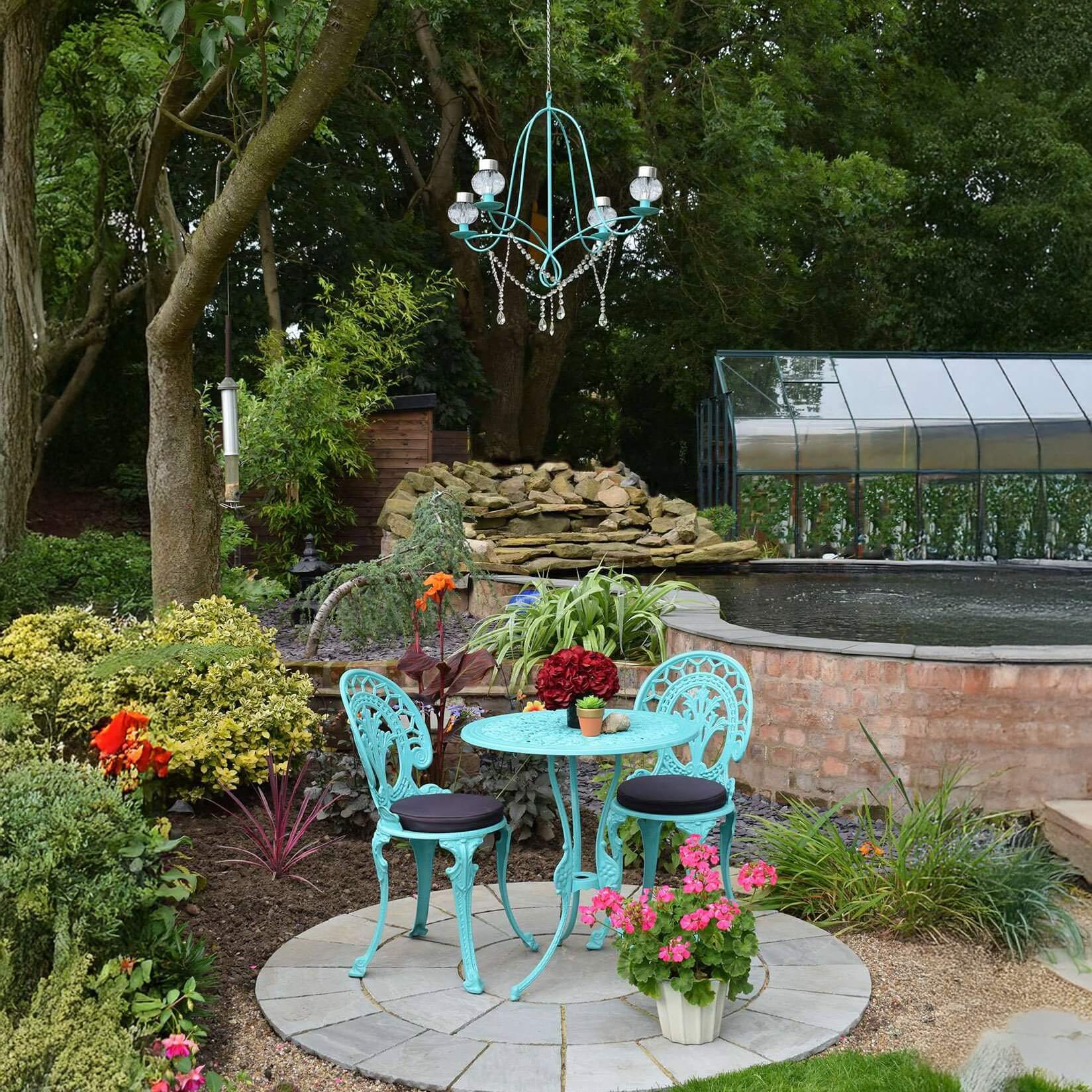 Turquoise outdoor chandelier with crystal drops hangs above a small garden bistro set beside a pond.