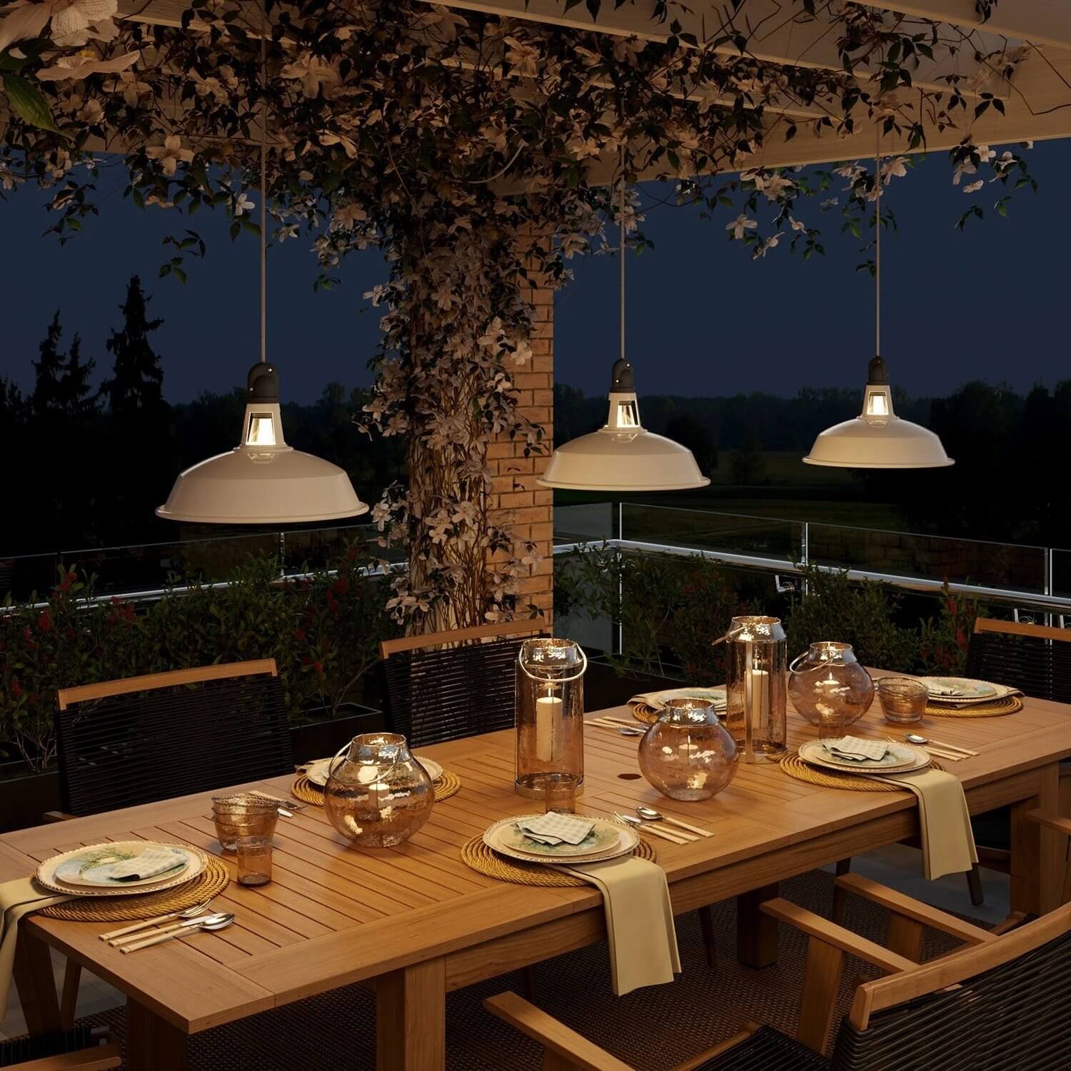 Covered outdoor dining area with white industrial pendant lights over a large wooden table set for an evening gathering.