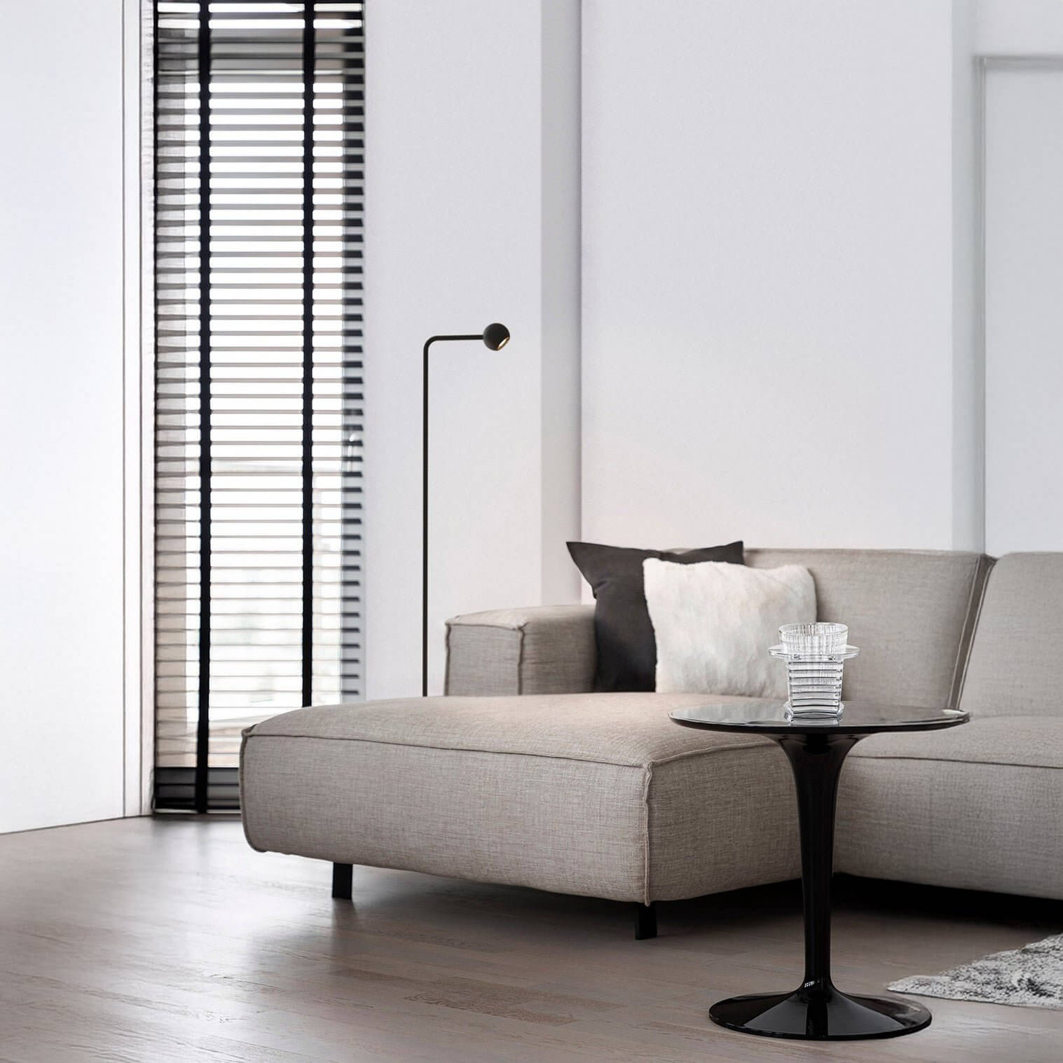 Slim black minimalist floor lamp with tiny round head next to a beige sectional sofa.