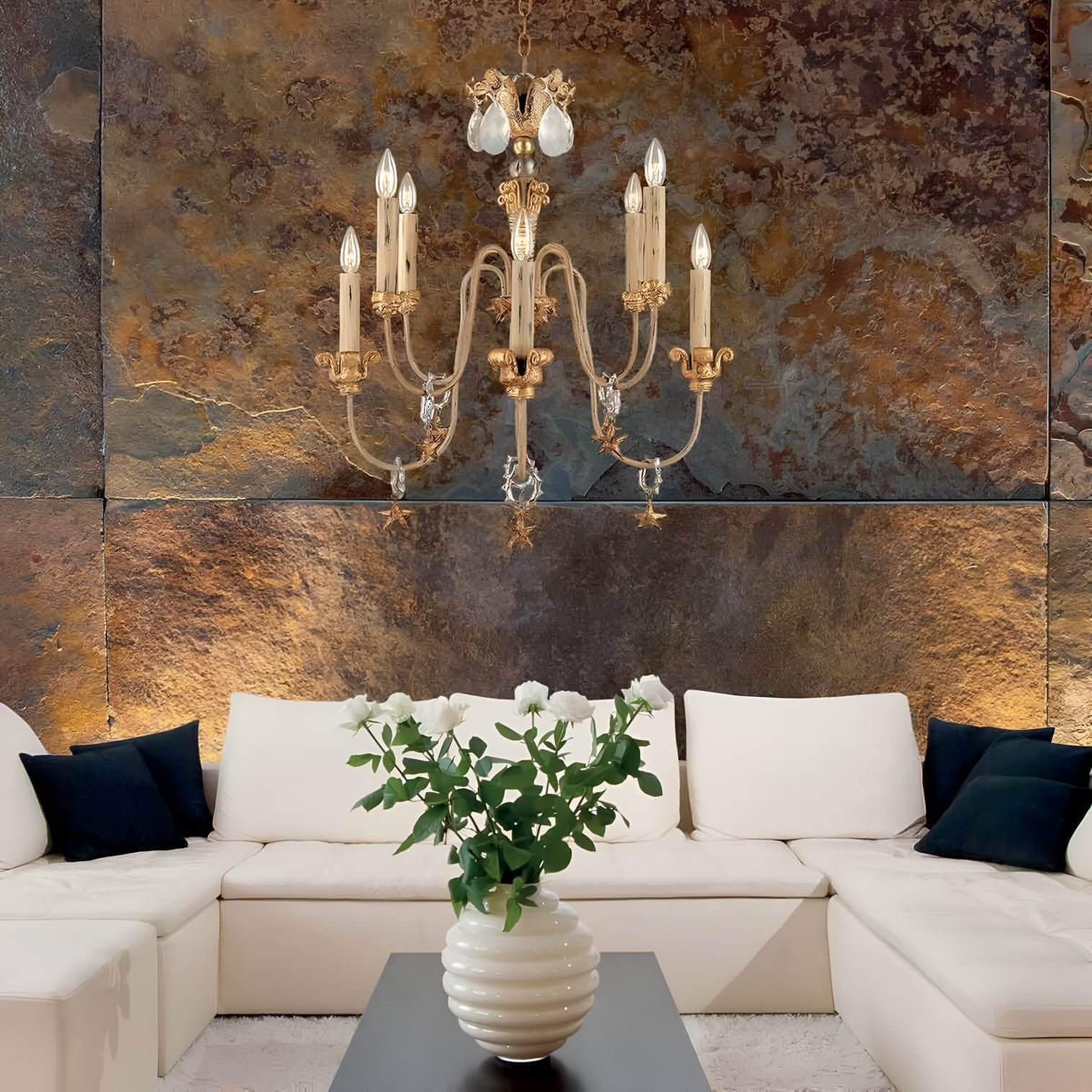 Gold crystal chandelier above a white sectional sofa set against a textured stone wall in a warm-toned living room.