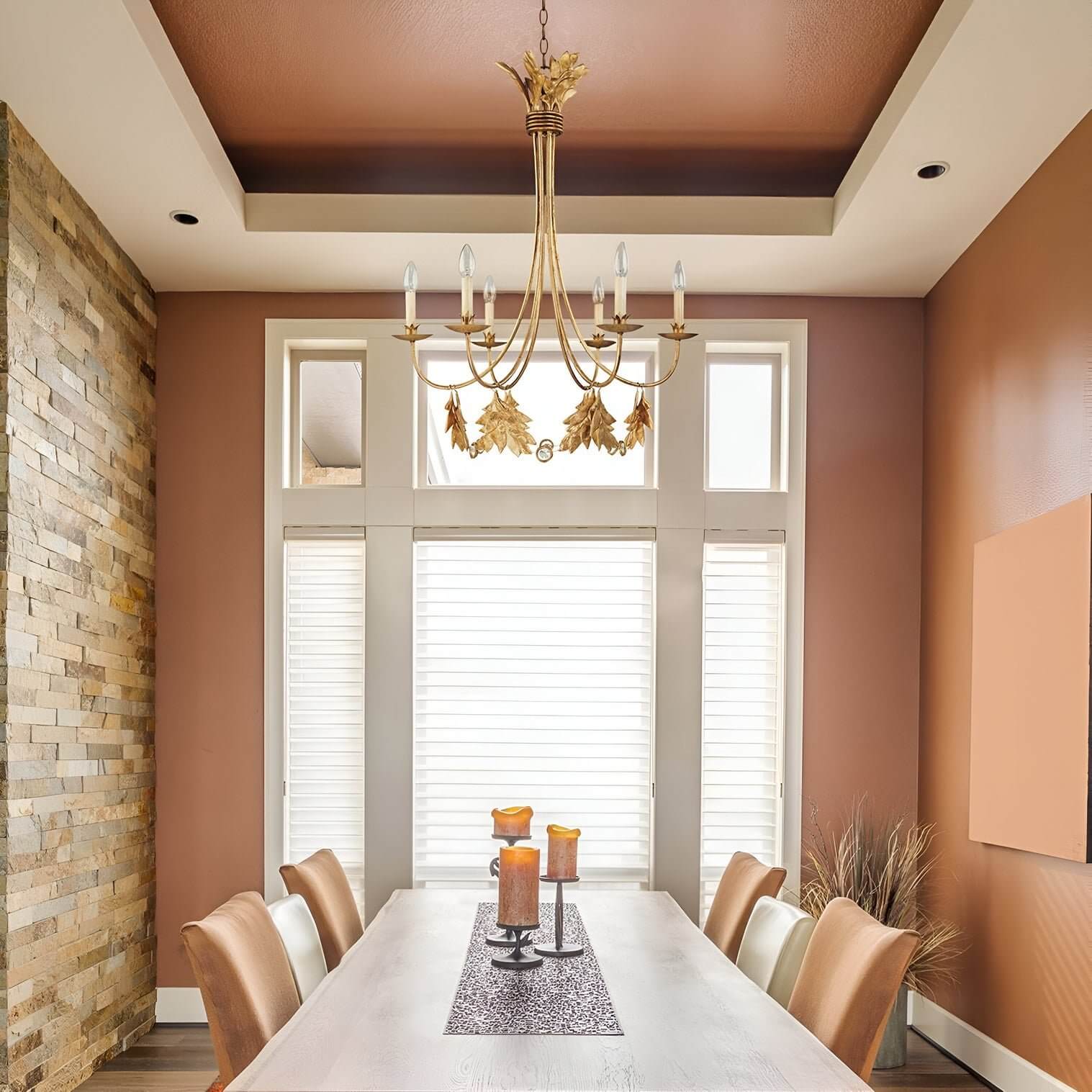 Dining room with warm earthy walls, tall windows, and a gold chandelier with candle-style bulbs and leaf details.