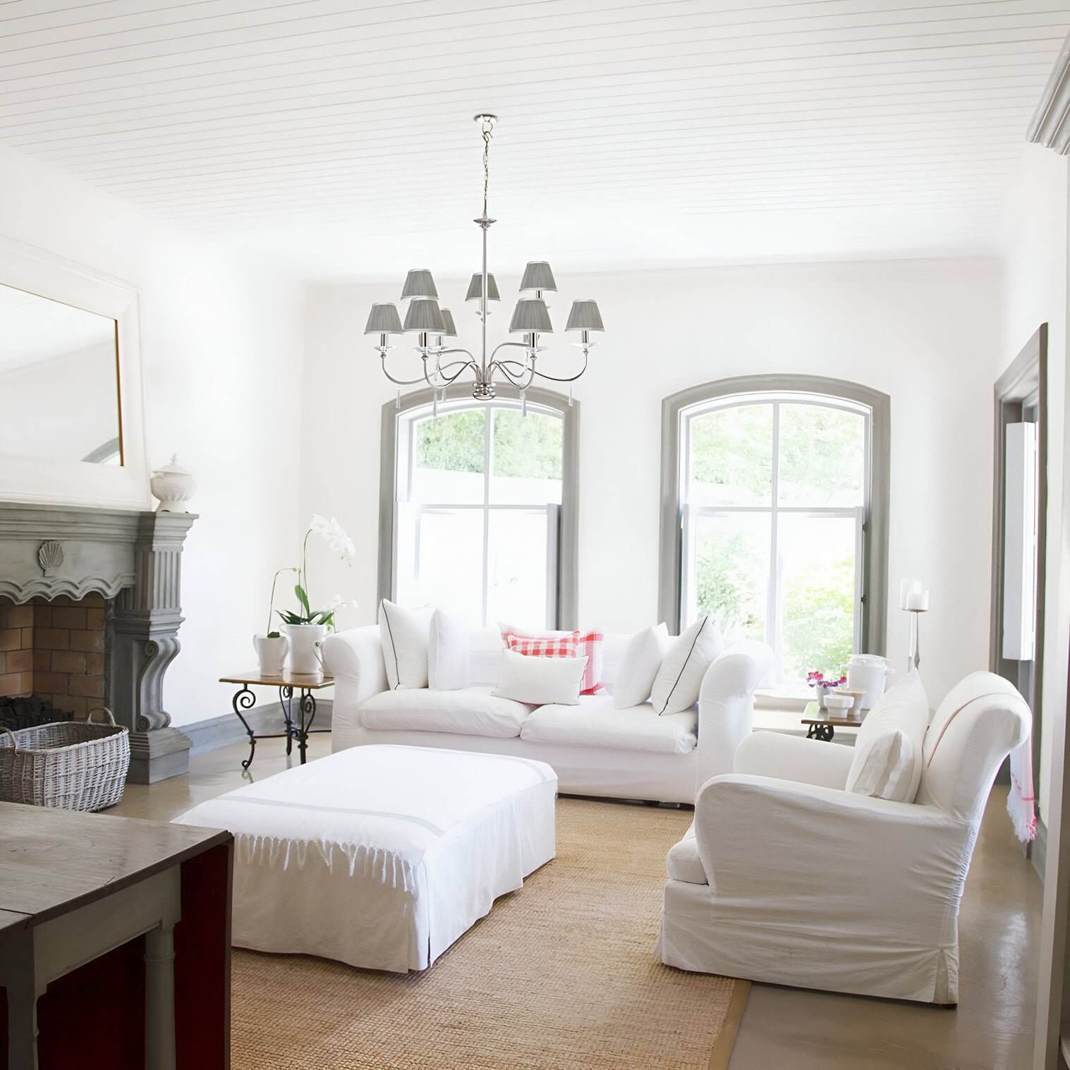 Elegant gray-shaded chandelier in a white living room with slipcovered seating and arched windows.