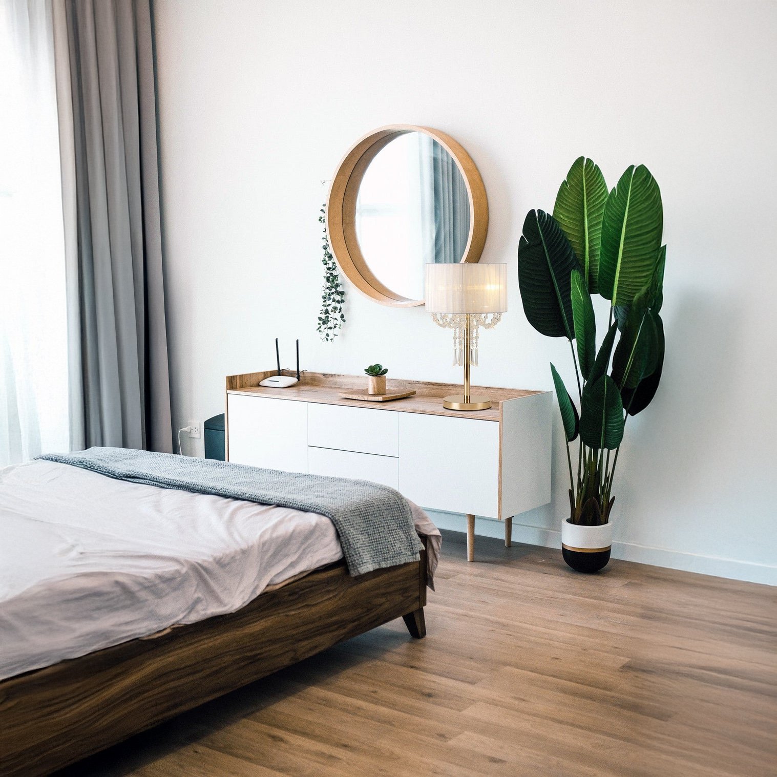 Minimal bedroom with a gold crystal table lamp on a white sideboard beside a large plant.