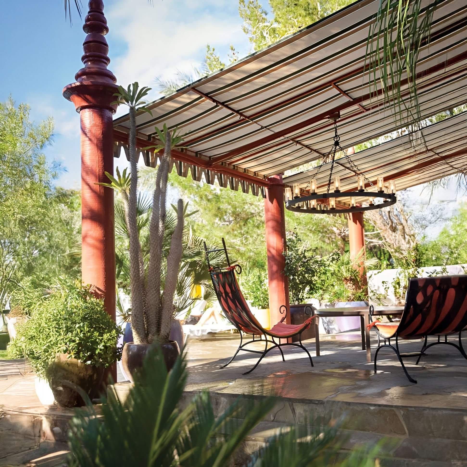 Large round wagon wheel chandelier with candle-style bulbs under a striped pergola in a tropical patio.