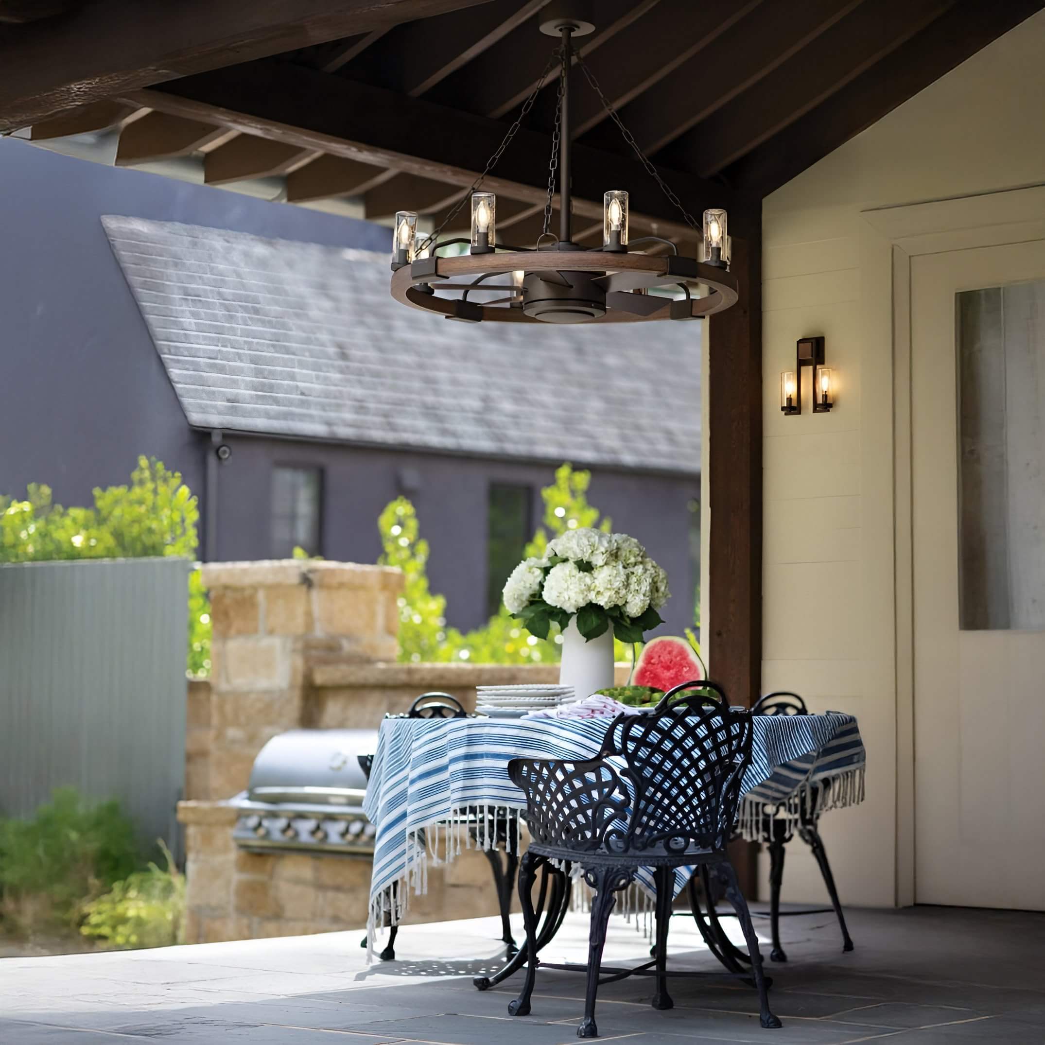 Rustic circular chandelier with glass-shaded bulbs hangs over a covered outdoor dining area.