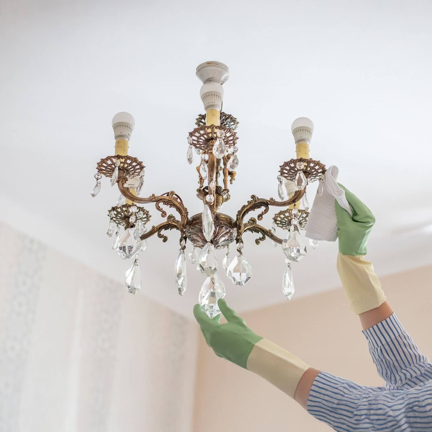 Person cleaning vintage crystal chandelier with gloves and a microfiber cloth.