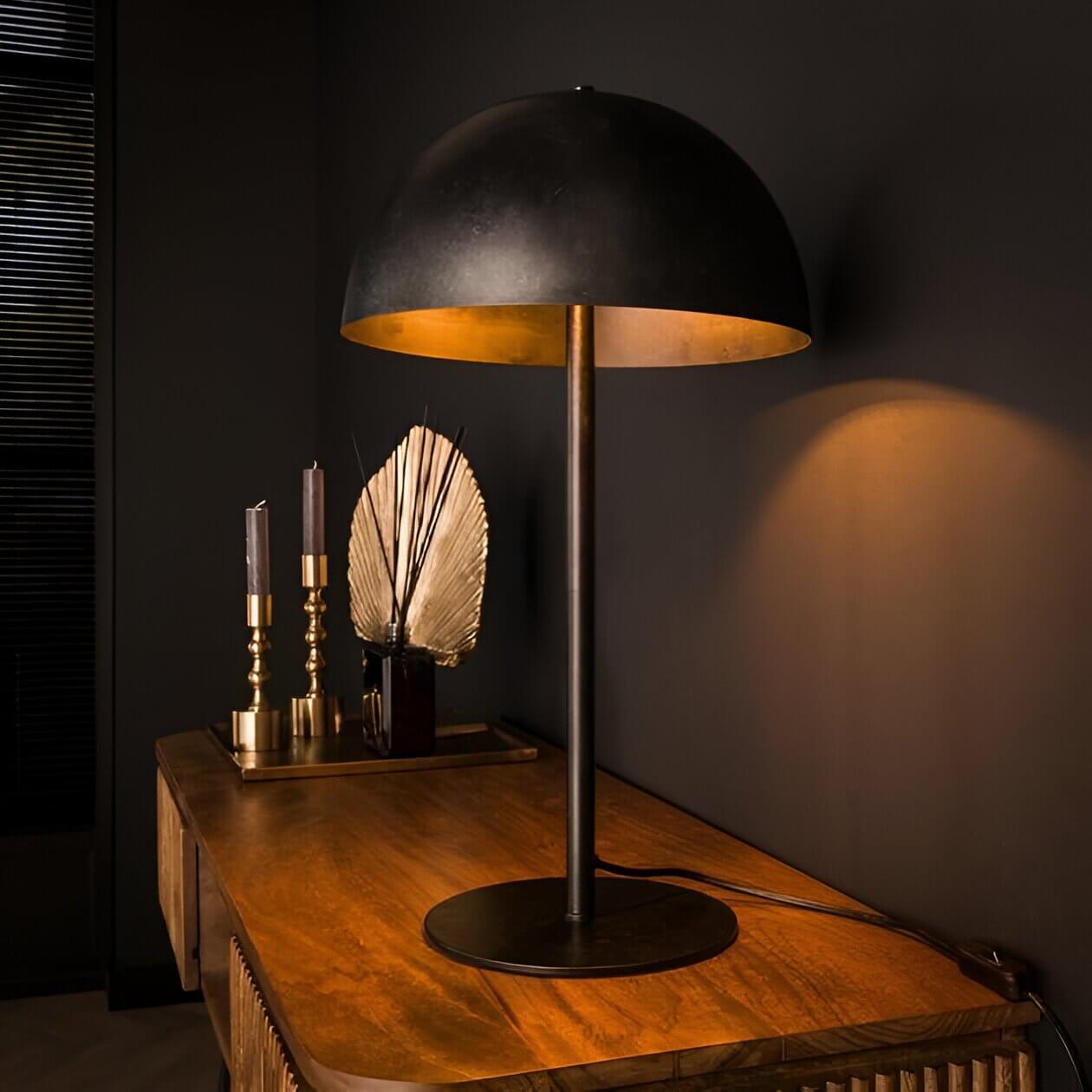 Matte black dome table lamp with gold inner shade on a wooden console in a moody, dark-toned interior.