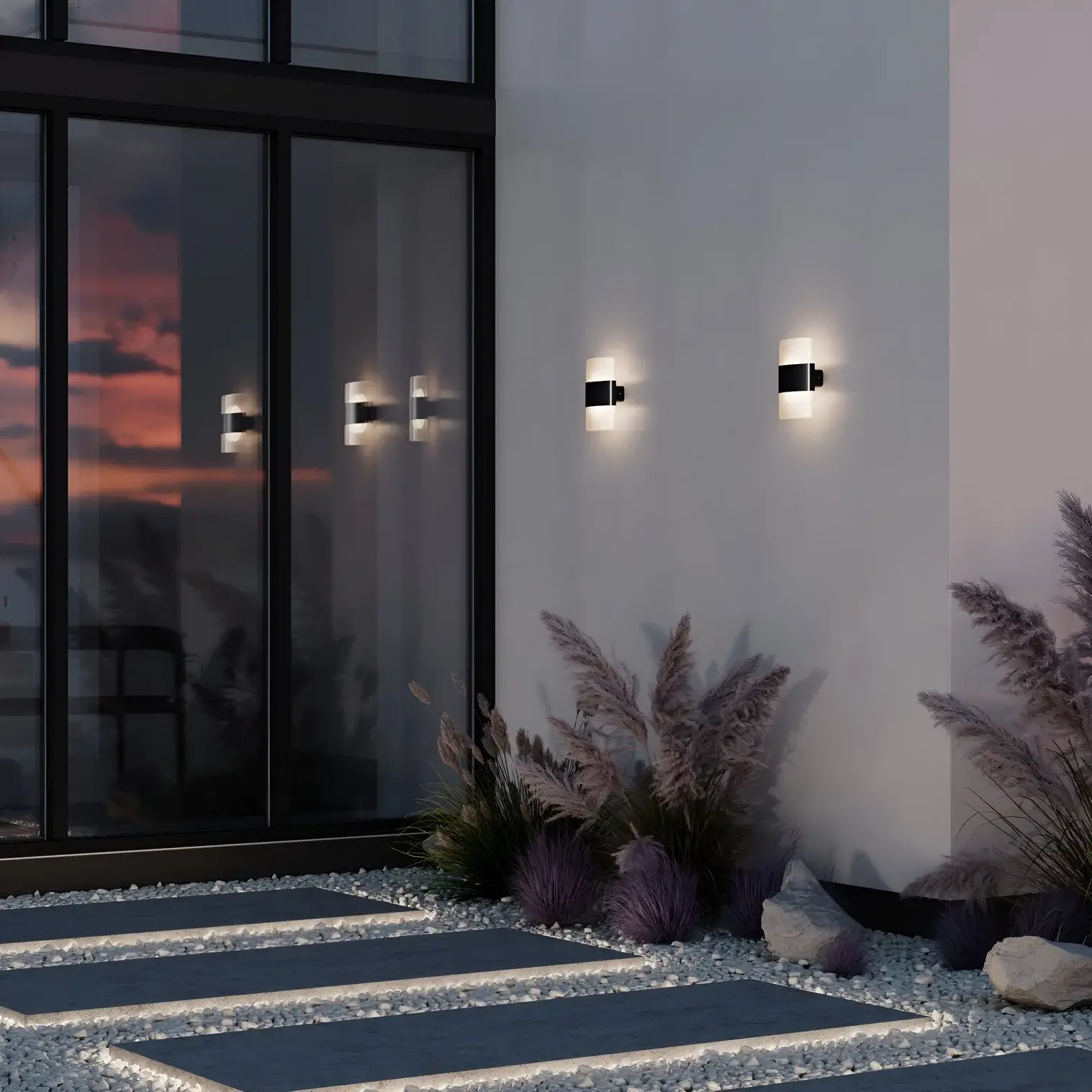 Evening view of a modern patio with black and white wall sconces glowing against a glass façade and decorative gravel garden.