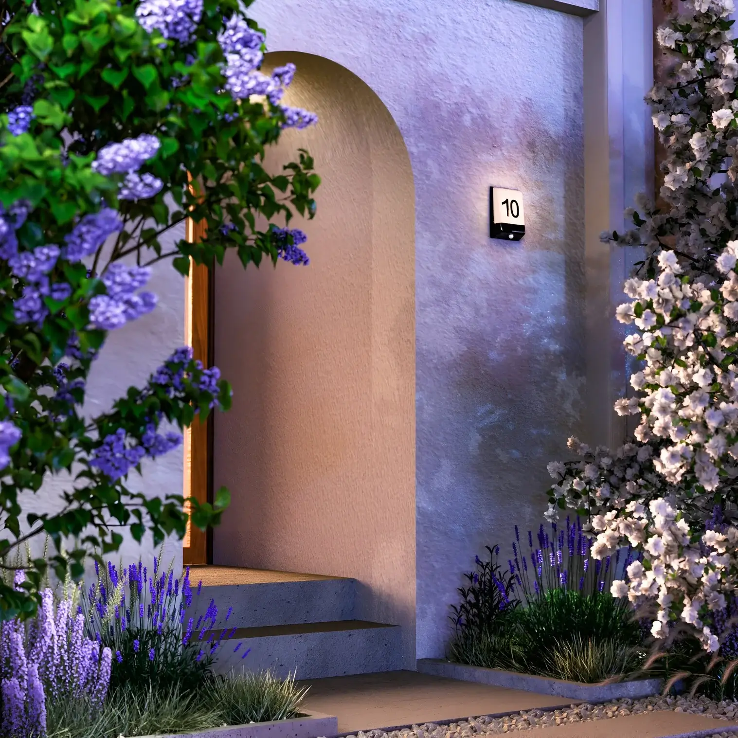Front door entrance lit by a square wall light with number 10, framed by blooming trees and purple garden flowers.