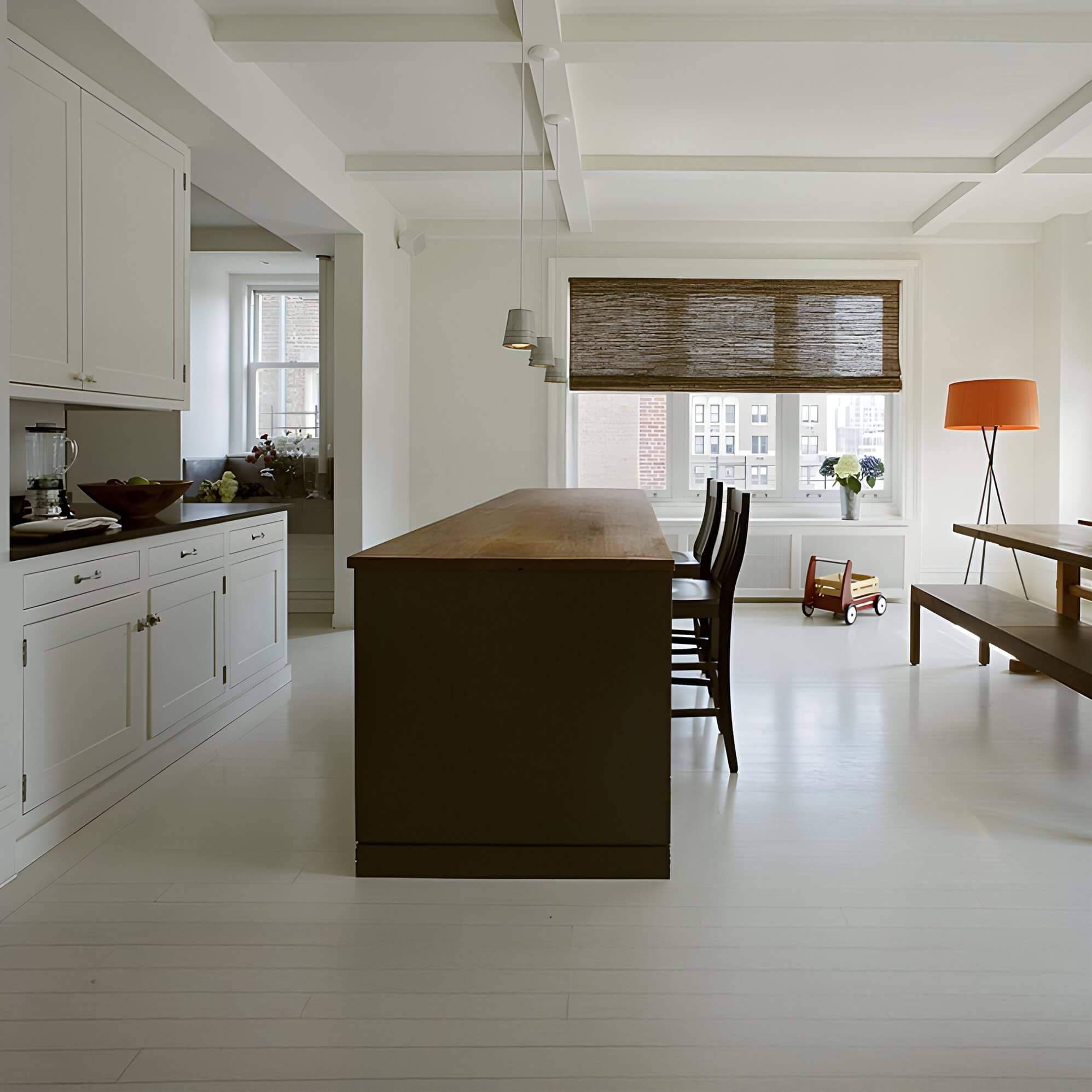Minimalist kitchen with brown island, white floors, and orange floor lamp near window seat.