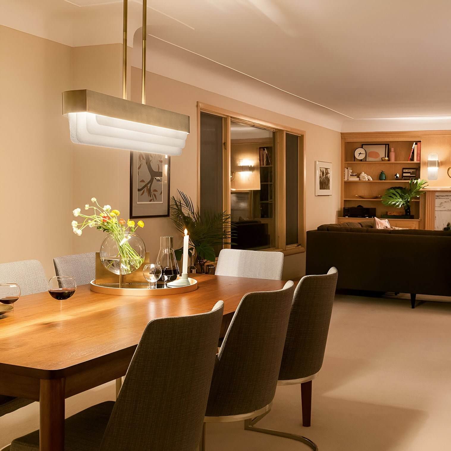 Rectangular pendant light with layered diffuser suspended over a wood dining table in a warm-toned open-plan living space.