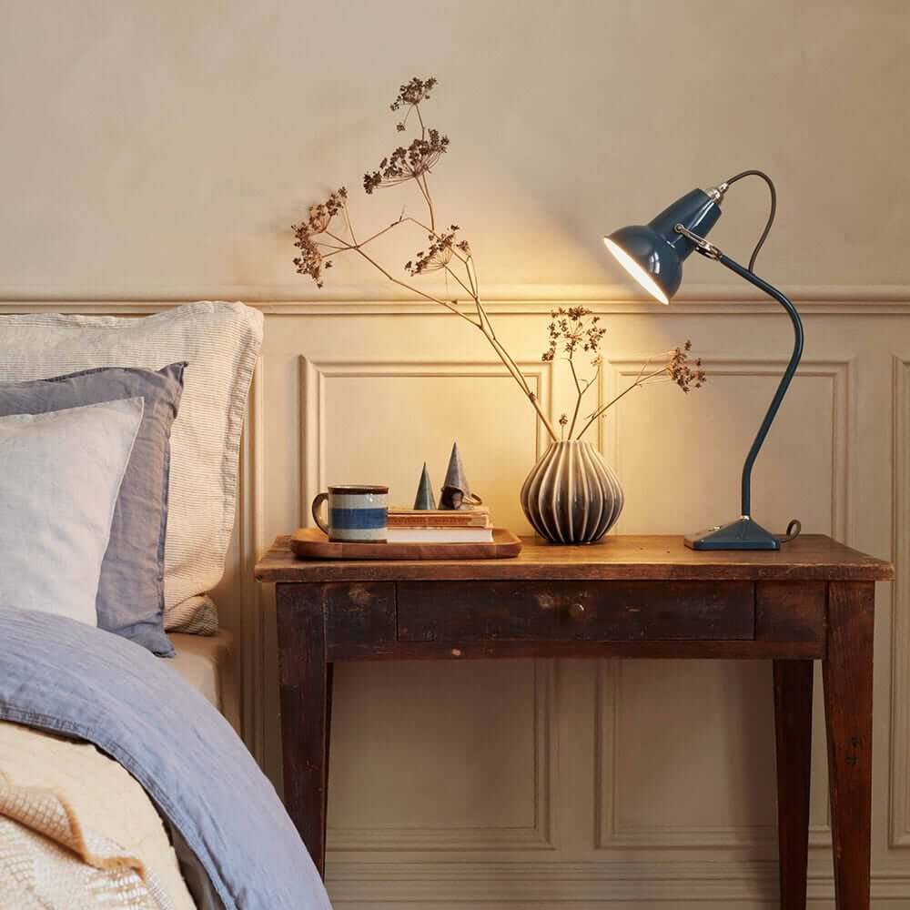 Navy blue reading lamp on a rustic wooden bedside table, styled with dried flowers and stacked books.