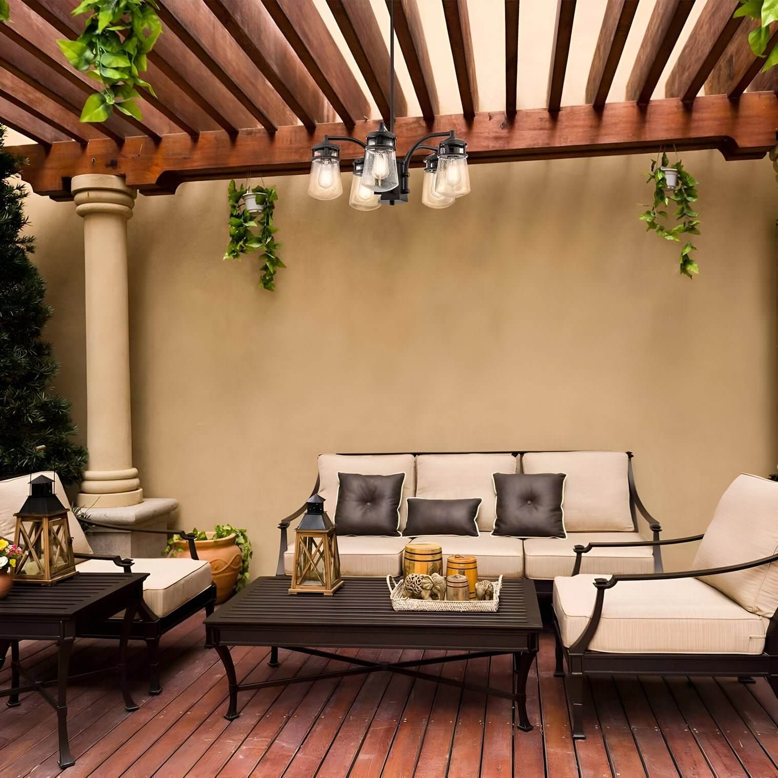 Black outdoor chandelier with five glass shades hanging under a wooden pergola in a neutral-toned patio seating area.