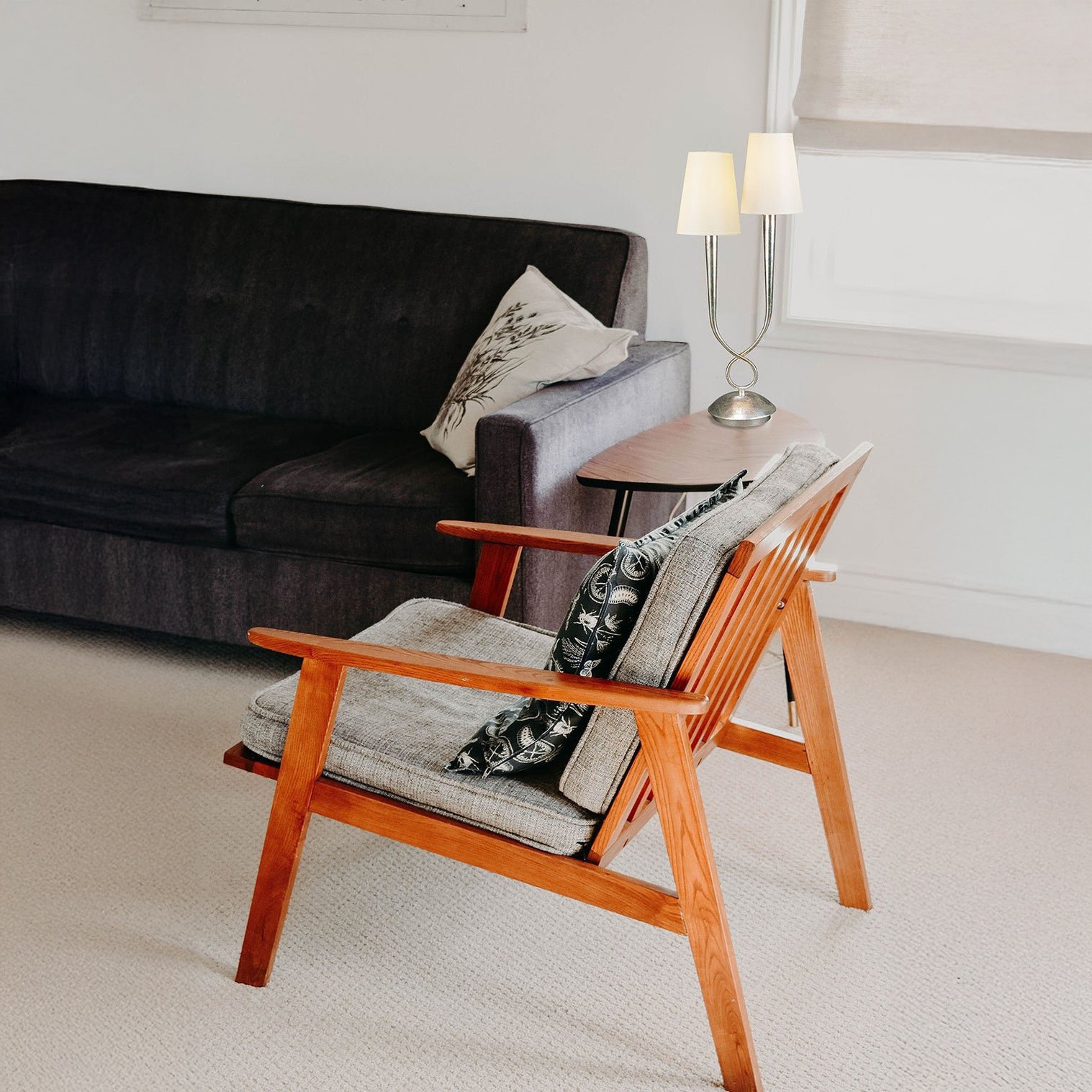 Mid-century living room with a dual-shade silver table lamp beside a wooden armchair.
