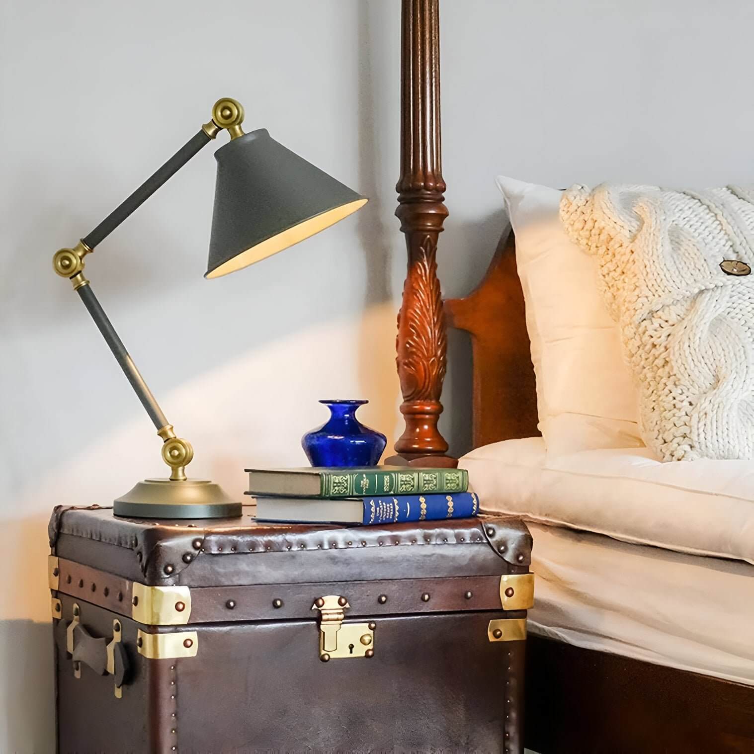Vintage-style desk lamp with brass accents on leather trunk nightstand beside carved wood bed