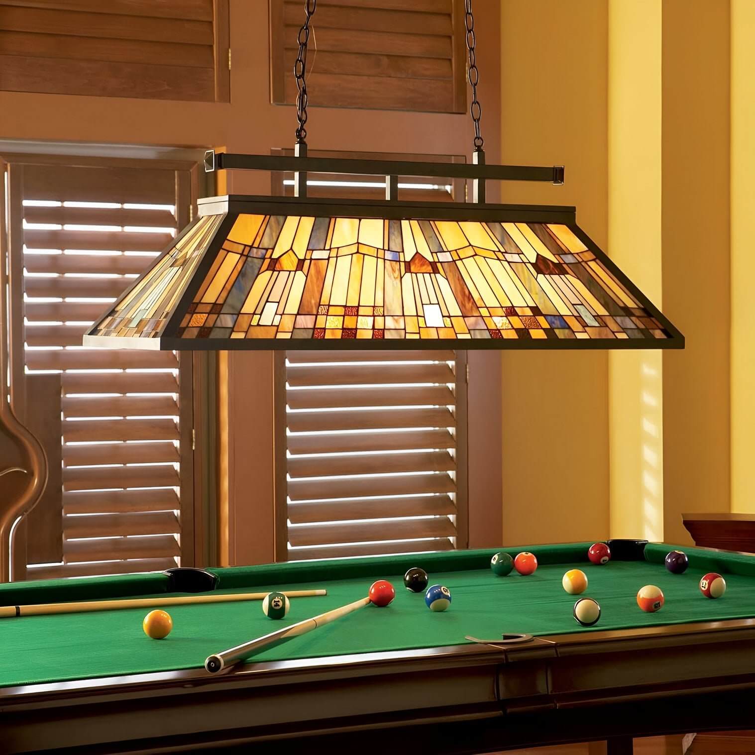 Rectangular Tiffany-style pendant light over pool table with geometric stained glass in warm amber and gold tones