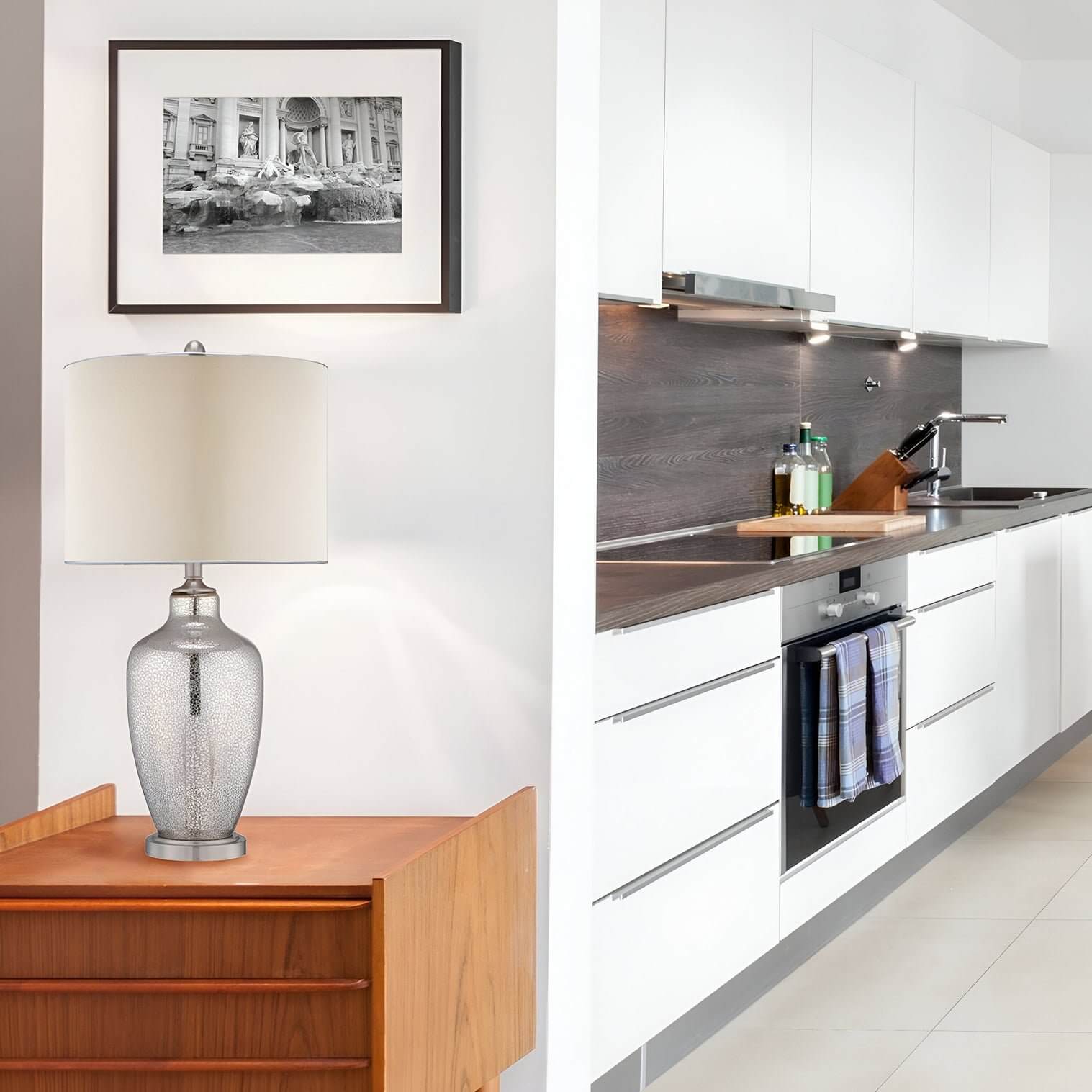 Textured metallic lamp with fabric shade on teak cabinet near white kitchen cabinetry