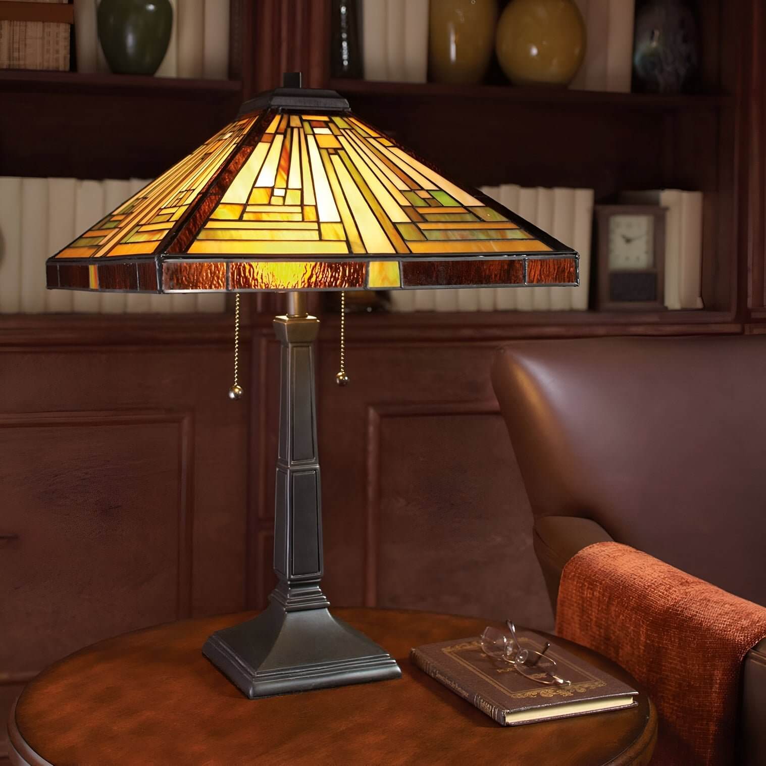 Tiffany-style stained glass lamp on wood side table beside leather armchair & book