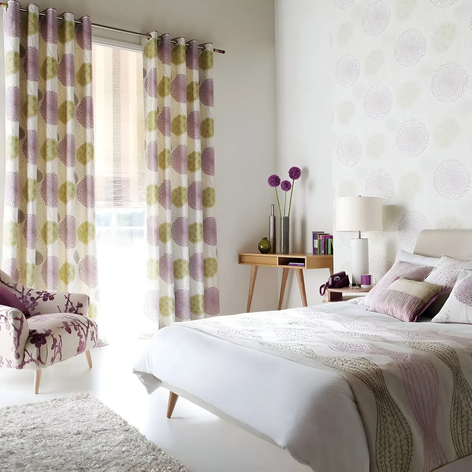 A light-filled bedroom showcasing pastel and floral accents, with a neatly made bed, a side table with decorative elements, patterned curtains, and a floral armchair.