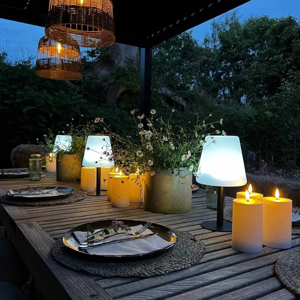Cone-shaped portable table lamps on a rustic outdoor dining table with candles and flower arrangements at dusk.