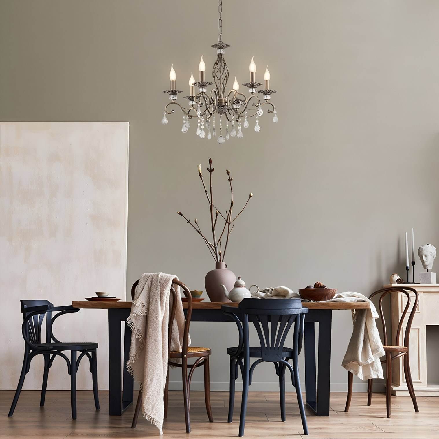 Iron chandelier with candle bulbs over a rustic dining table set with eclectic wooden chairs.
