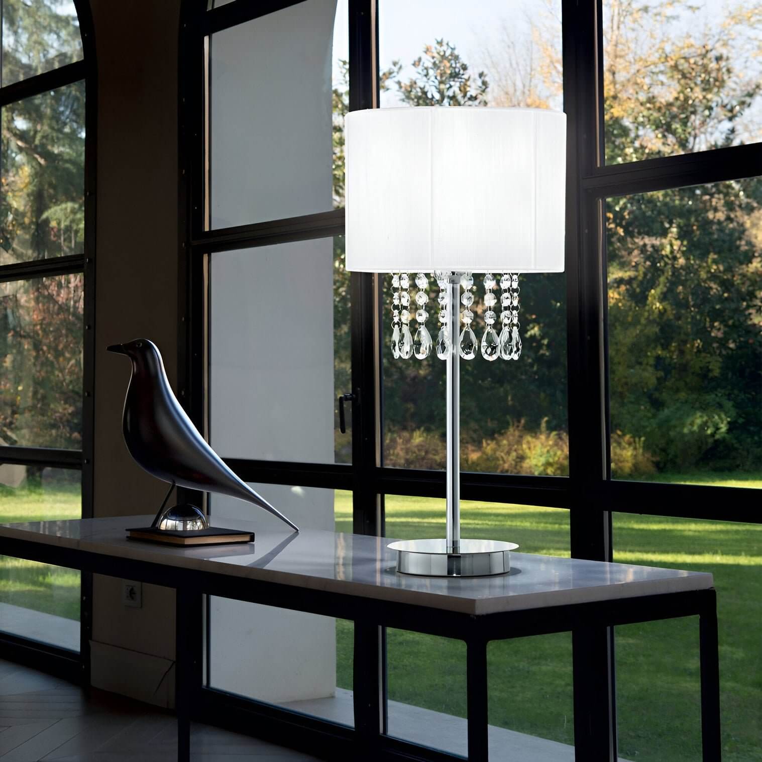 a  Crystal-trimmed table lamp on black console by full-height window with black bird sculpture