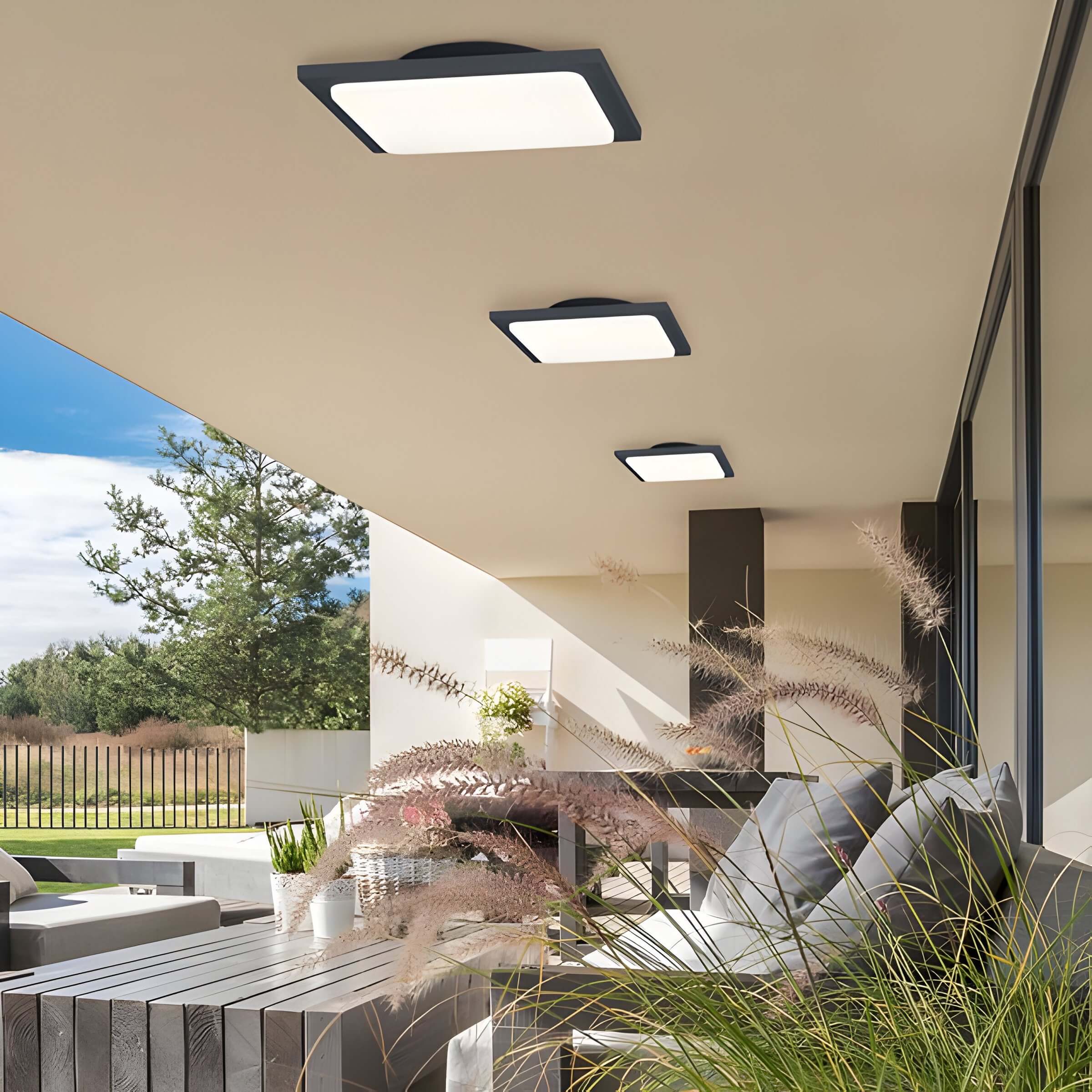 Modern outdoor lounge with square LED ceiling fixtures, low seating, and ornamental grass lining the patio.