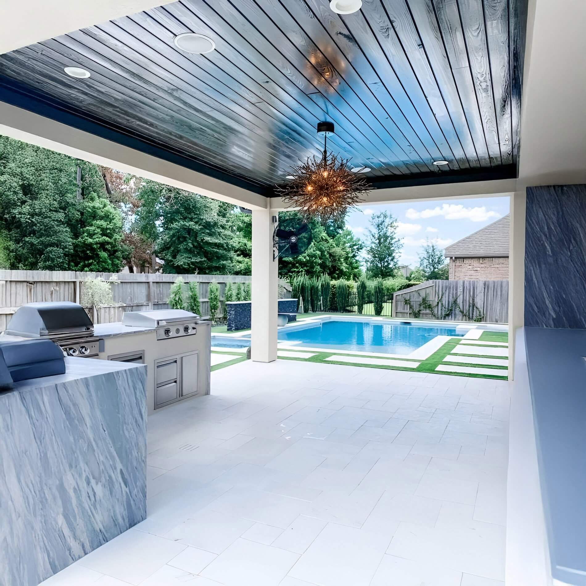 Modern starburst pendant light with multiple rods hangs over a covered poolside kitchen area.