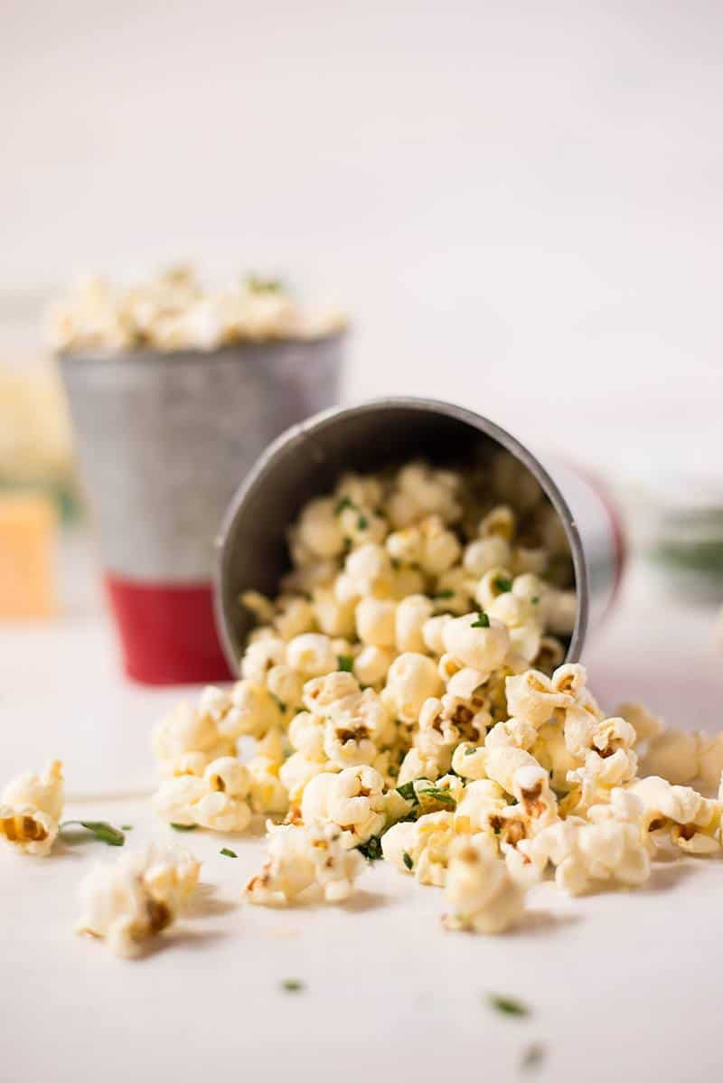 A photo of Healthy Homemade Popcorn Recipe on the counter falling out of a tin container..