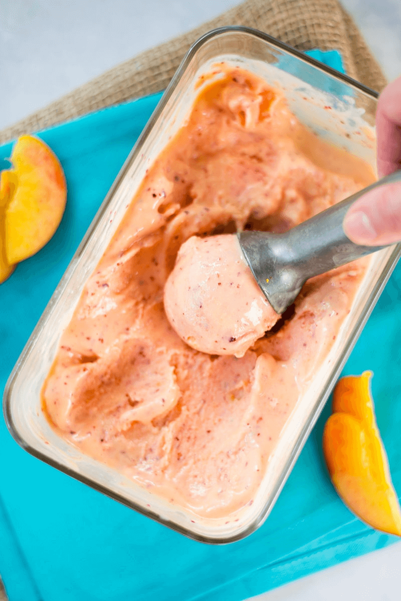 A photo of peach frozen yogurt in a clear glass container being scooped.
