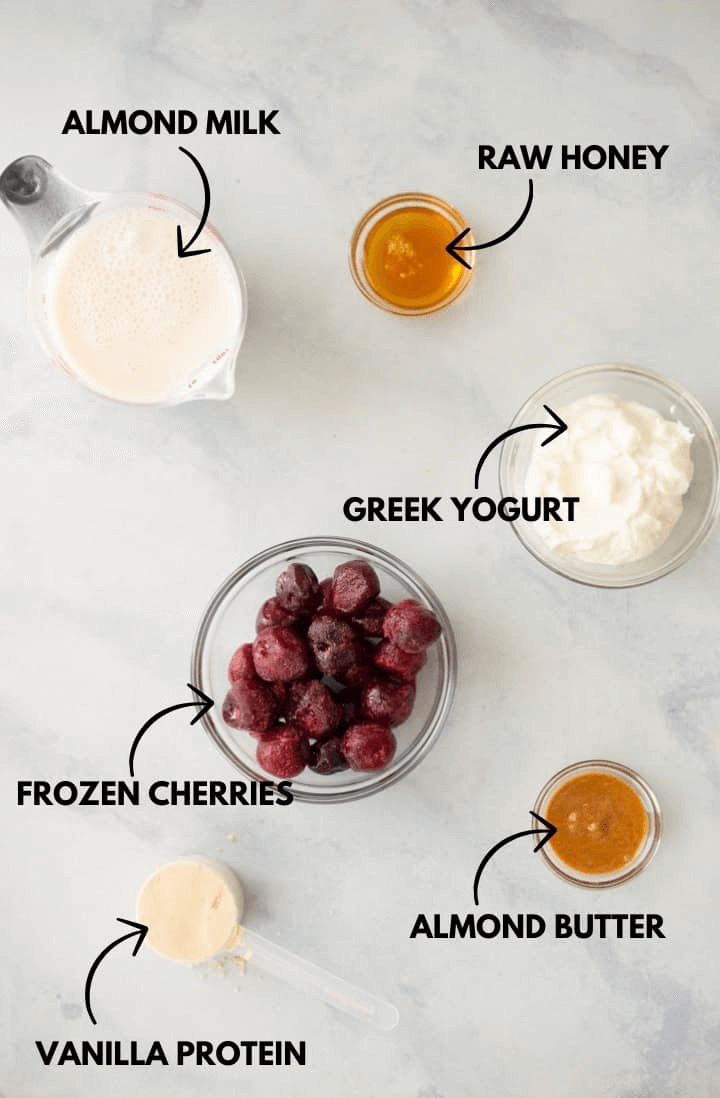 A photo of ingredients for cherry vanilla protein smoothie all laying flat against a white marble surface.