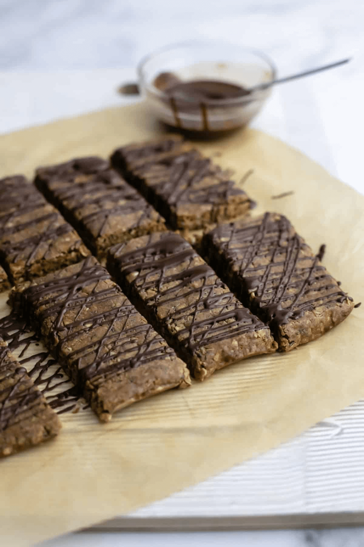 A photo of chocolate peanut butter protein bars on a piece of parchment paper with a chocolate drizzle.