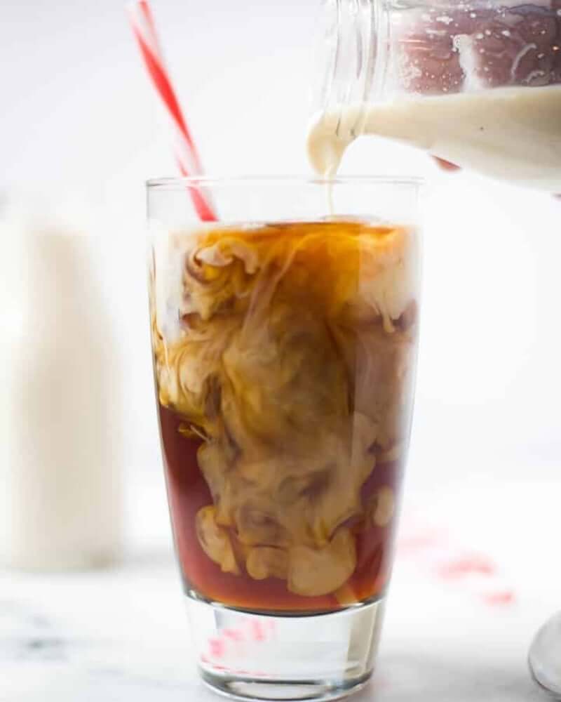 Creamer being poured into a clear glass cup of black coffee with a red and white striped straw.