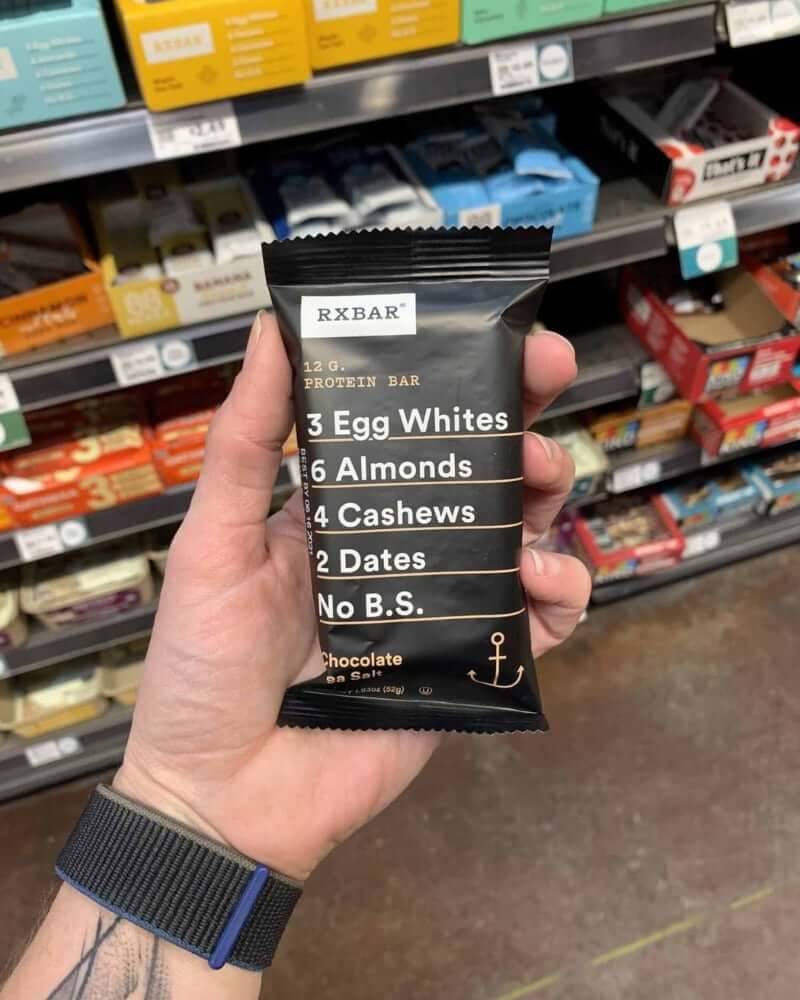 A hand holding a protein bar from the brand RXBar.