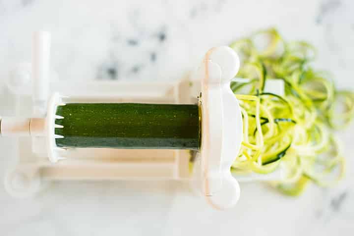Spiralizing zucchini with a veggie spiralizer to make zucchini noodles.