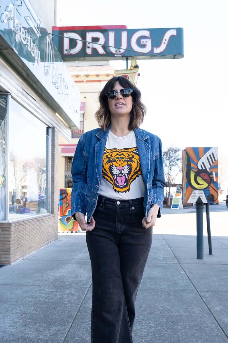 Angela wearing the Thread Hippie Cosmic Tiger women’s graphic tee styled with a vintage denim blazer and high-rise black jeans.