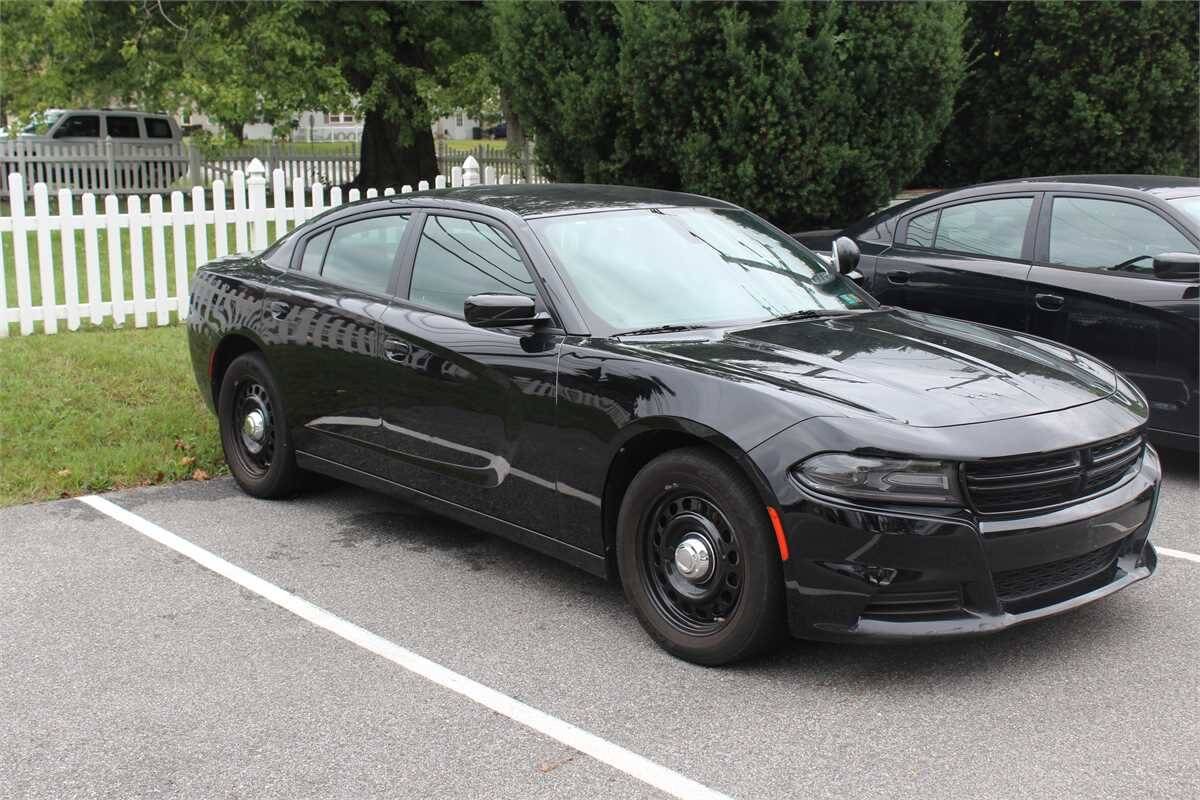 Black Dodge Charger in a parking lot in front of a white fence.