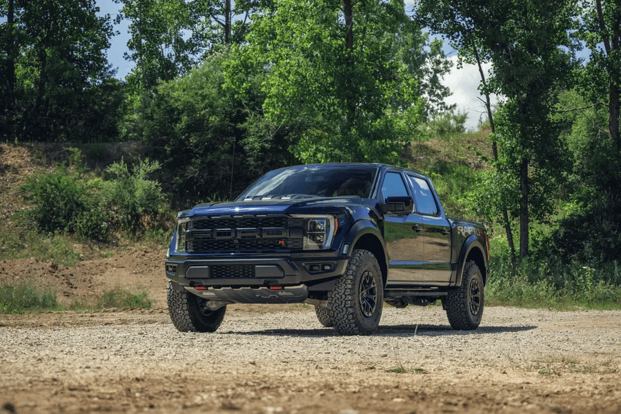 Black Ford F150 diesel vehicle parked in front of trees on a gravel road.